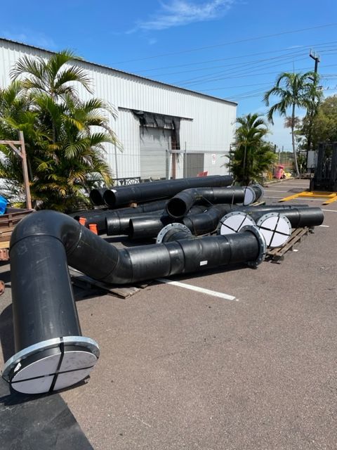 Large black duct pipes scattered across a parking lot beside a white industrial building — Advanced Poly in Darwin, NT