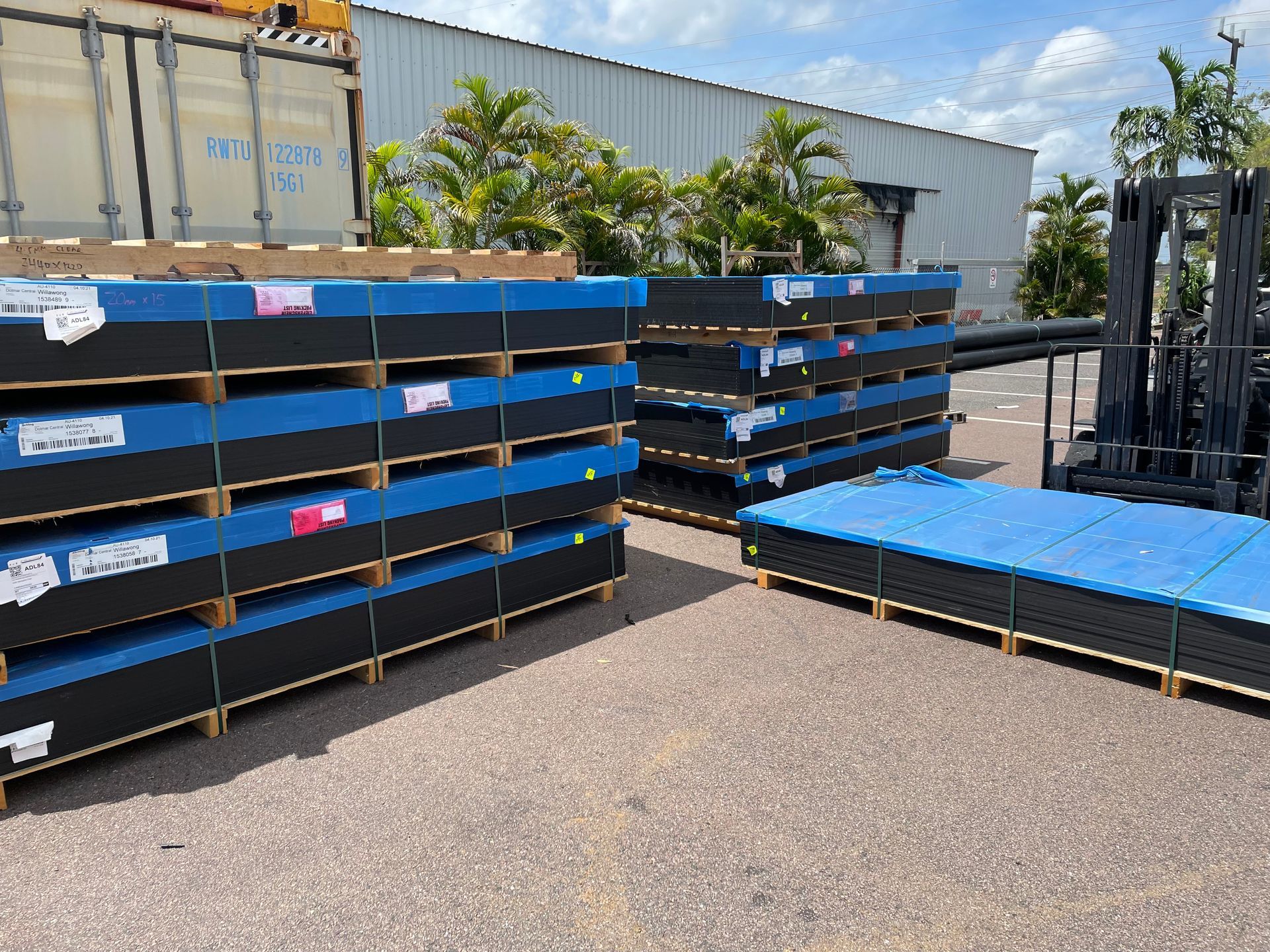 Stacks of blue-covered pallets in an outdoor industrial yard under a partly cloudy sky. — Advanced Poly in Darwin, NT — Advanced Poly in Darwin, NT 