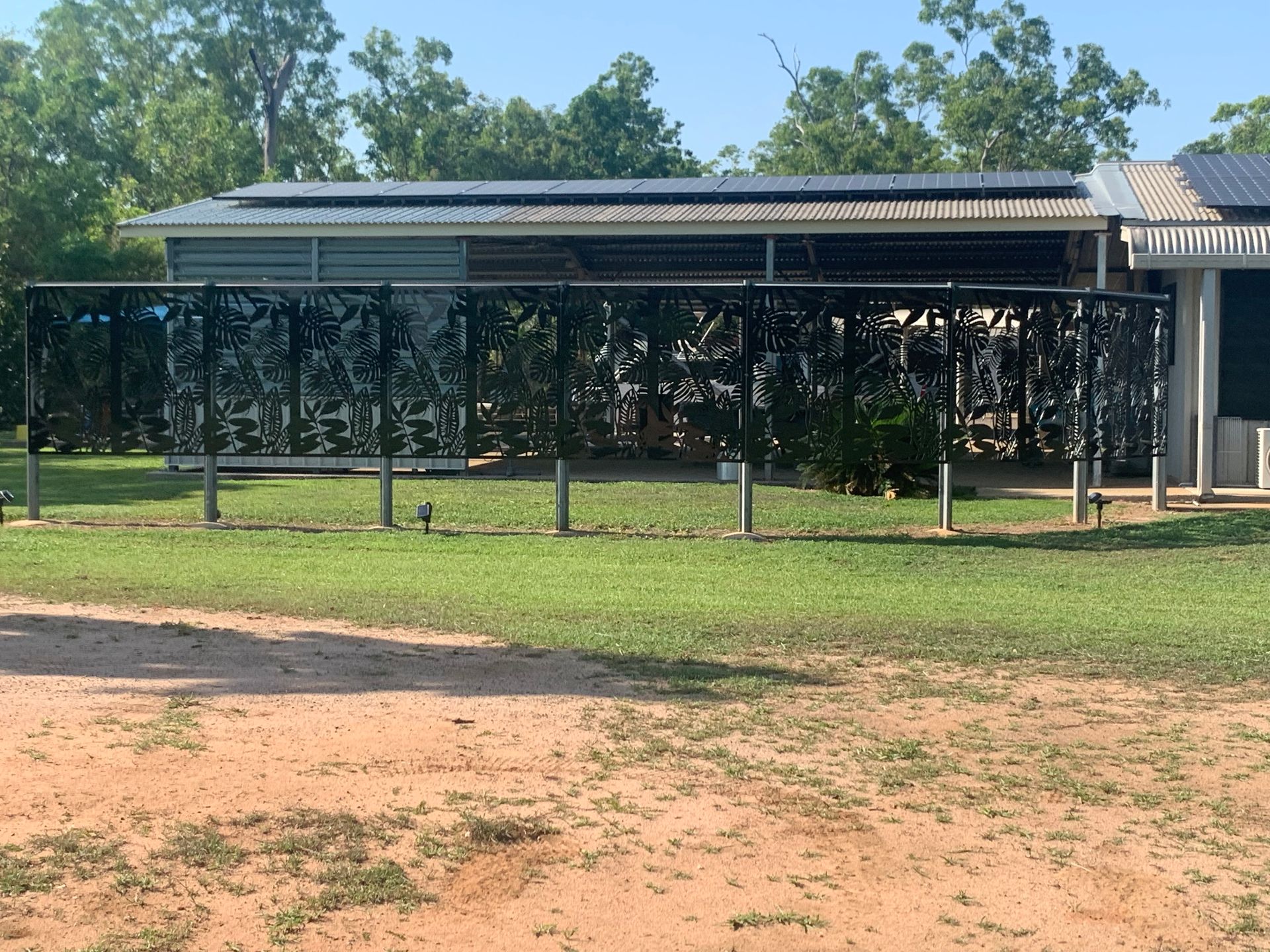 Long shaded outdoor shelter with mesh sides on a grassy field under a bright blue sky — Advanced Poly in Darwin, NT