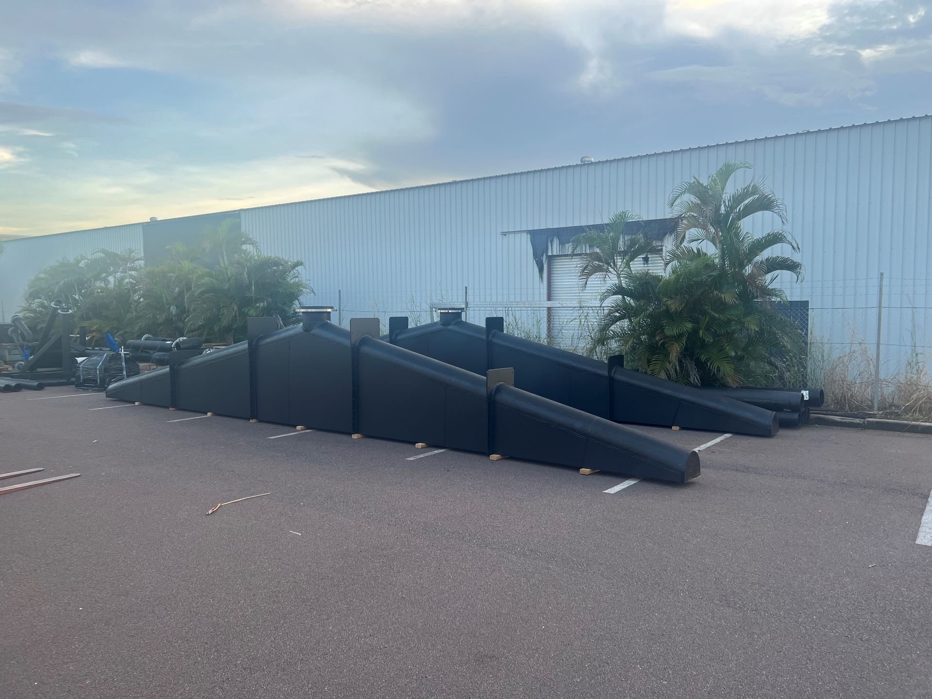 Black ramp and stair structure outside a white industrial building with palm trees and parking lot — Advanced Poly in Darwin, NT