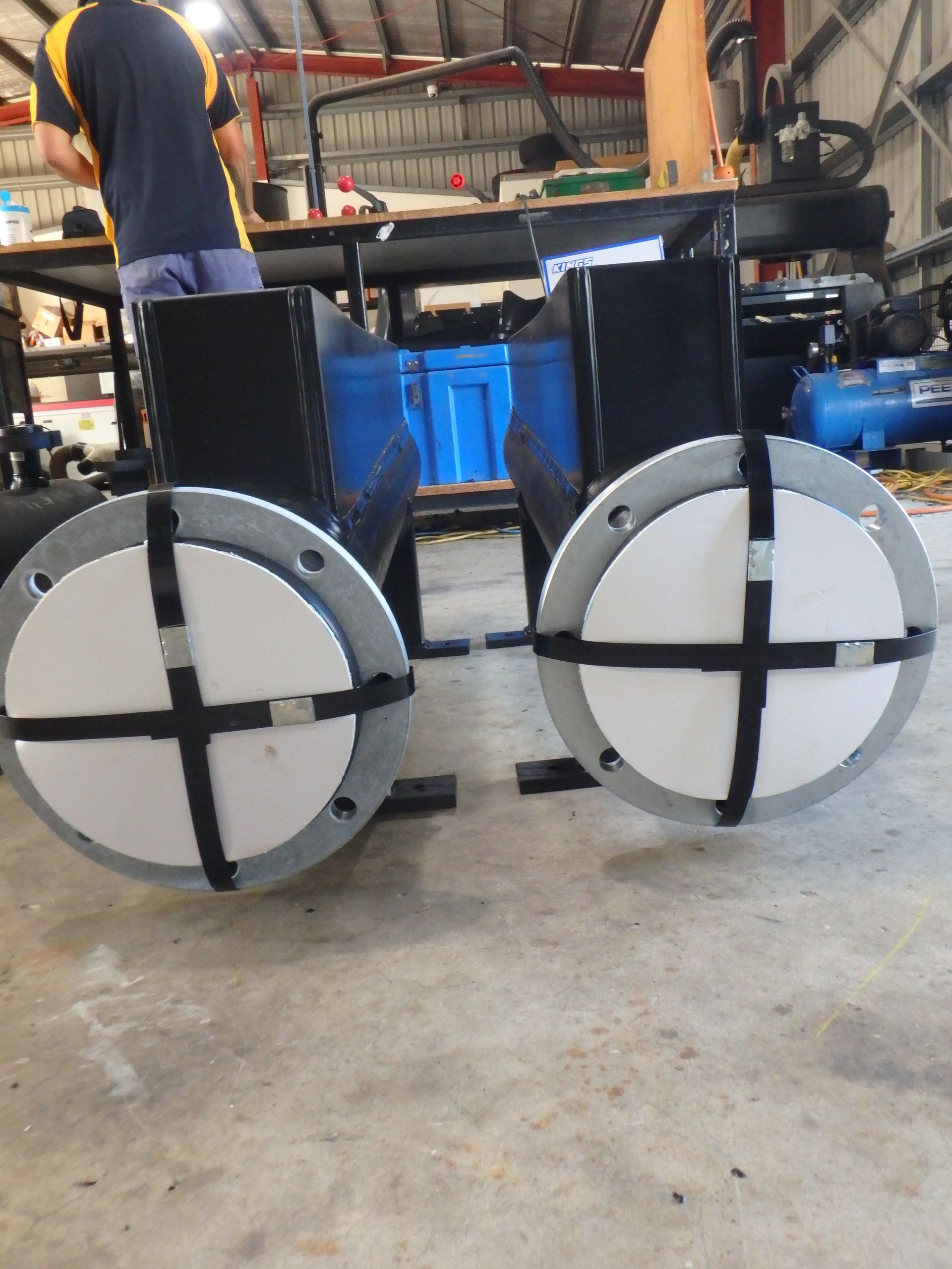 Two white circular wheeled devices with black cross braces in a workshop garage. — Advanced Poly in Darwin, NT — Advanced Poly in Darwin, NT 