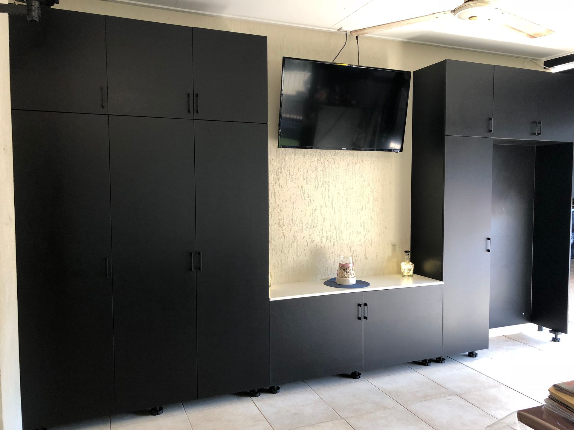 Modern kitchen with matte black cabinets, built-in TV, and beige backsplash; doors open to the right. — Advanced Poly in Darwin, NT