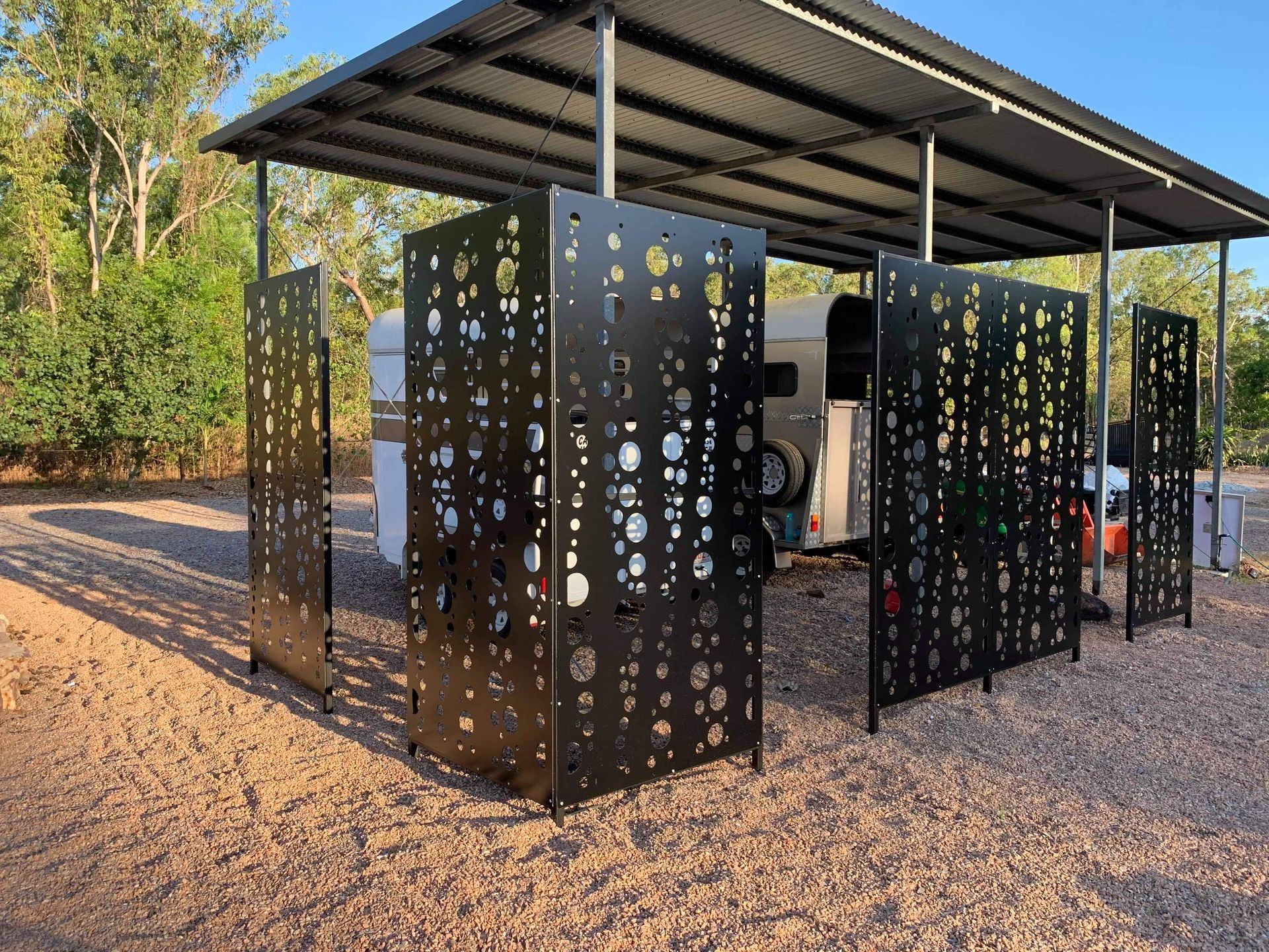Black metal shade shelter with perforated panels on a gravel lot in a wooded area — Advanced Poly in Darwin, NT