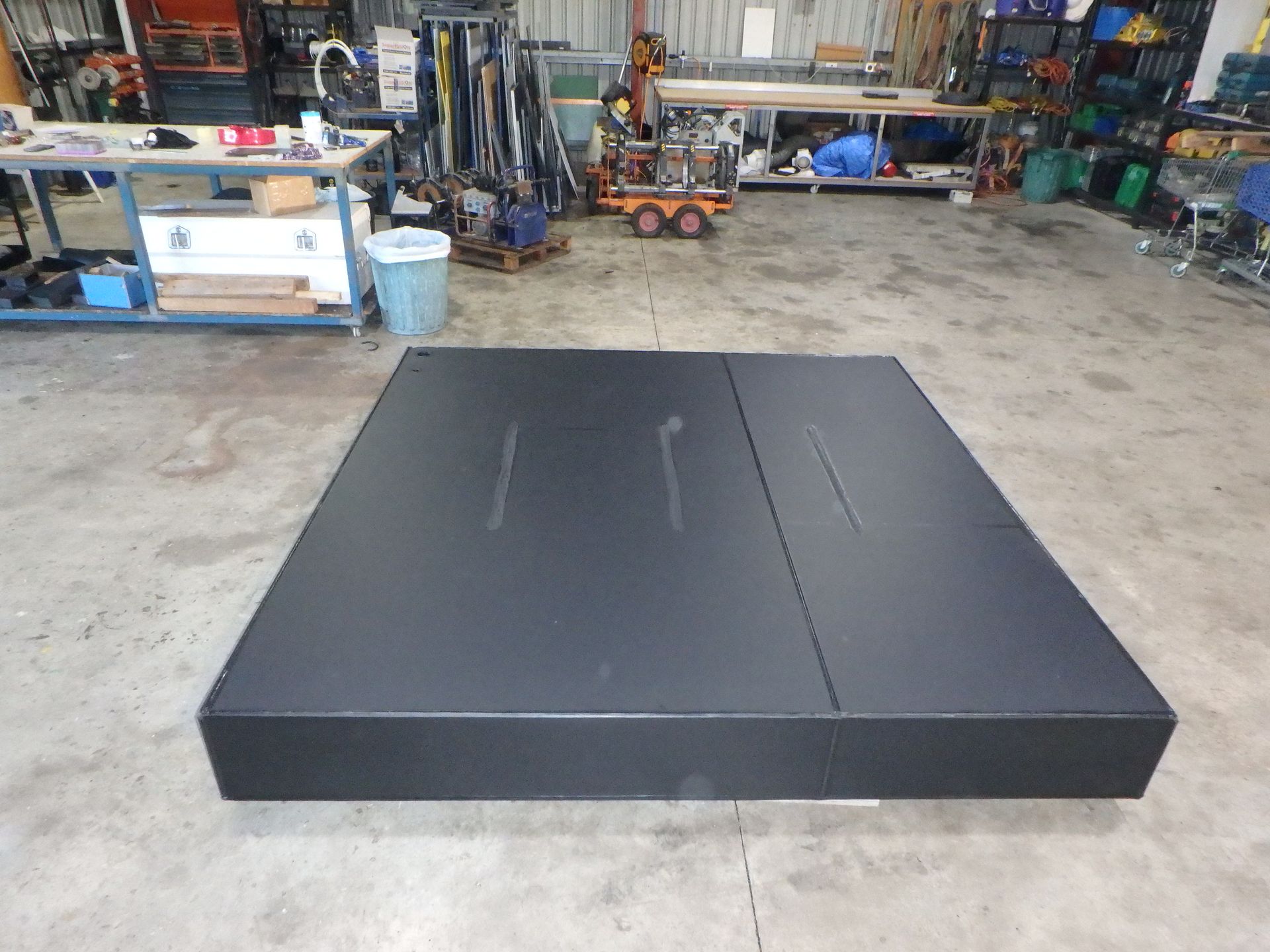 Large black rectangular platform in a workshop garage, with equipment and tools in the background. — Advanced Poly in Darwin, NT — Advanced Poly in Darwin, NT 