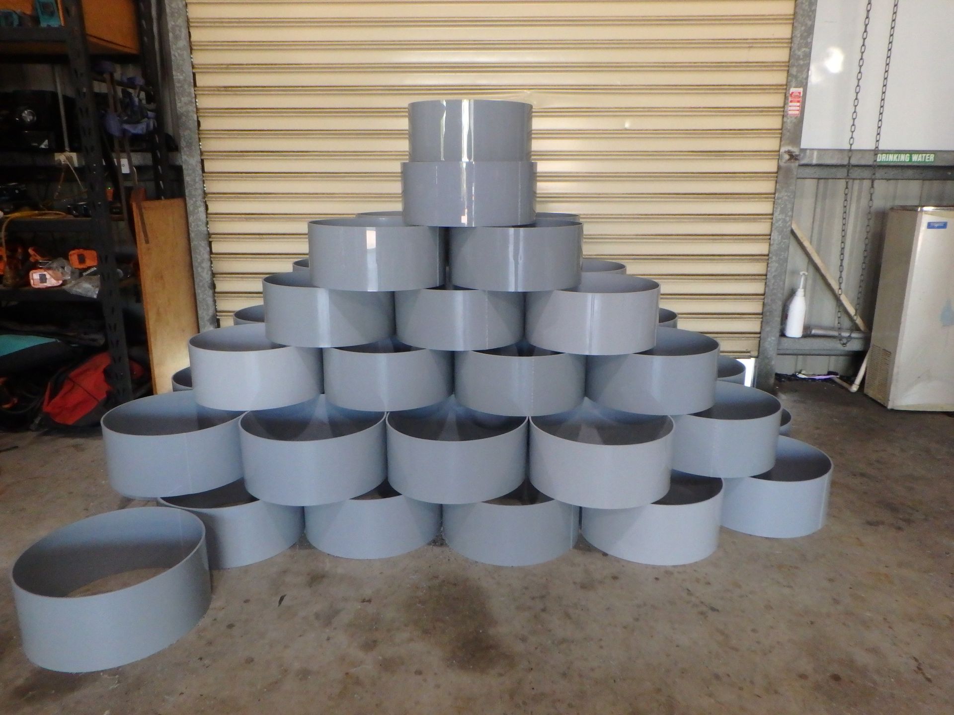 Stacked gray cylindrical metal parts arranged in a pyramid in an industrial garage. — Advanced Poly in Darwin, NT 