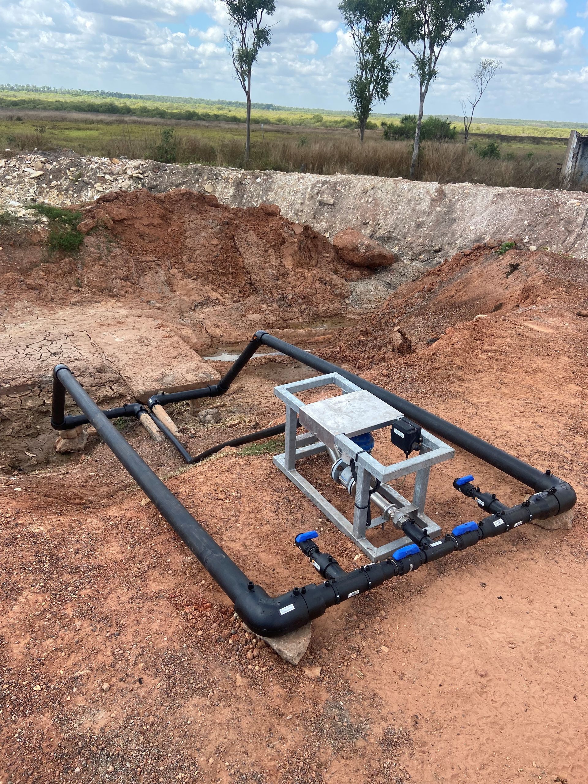 Black pipe frame with a small pump or control box in a muddy outdoor excavation area. — Advanced Poly in Darwin, NT