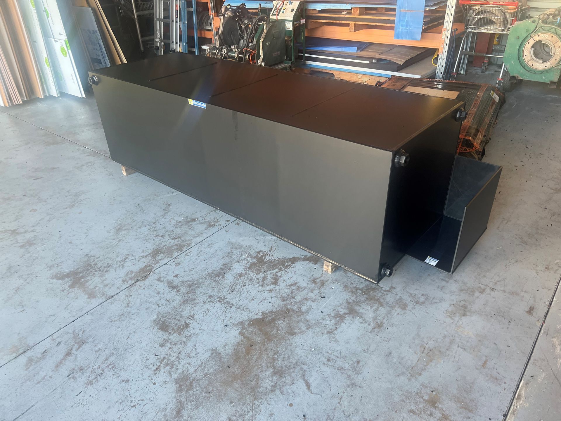 Black metal cabinet or equipment enclosure on a concrete floor in an industrial garage area — Advanced Poly in Darwin, NT