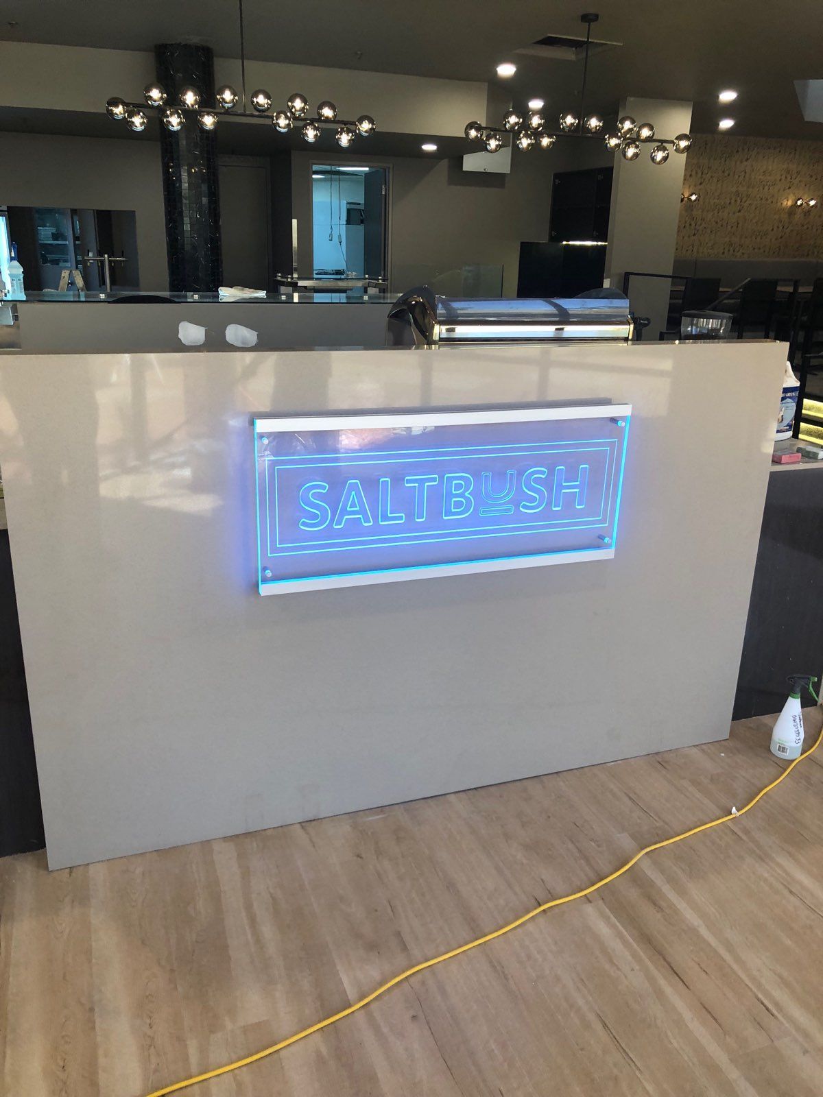 Modern café counter with a glowing blue sign and light wood floor; yellow cord runs across the foreground — Advanced Poly in Darwin, NT