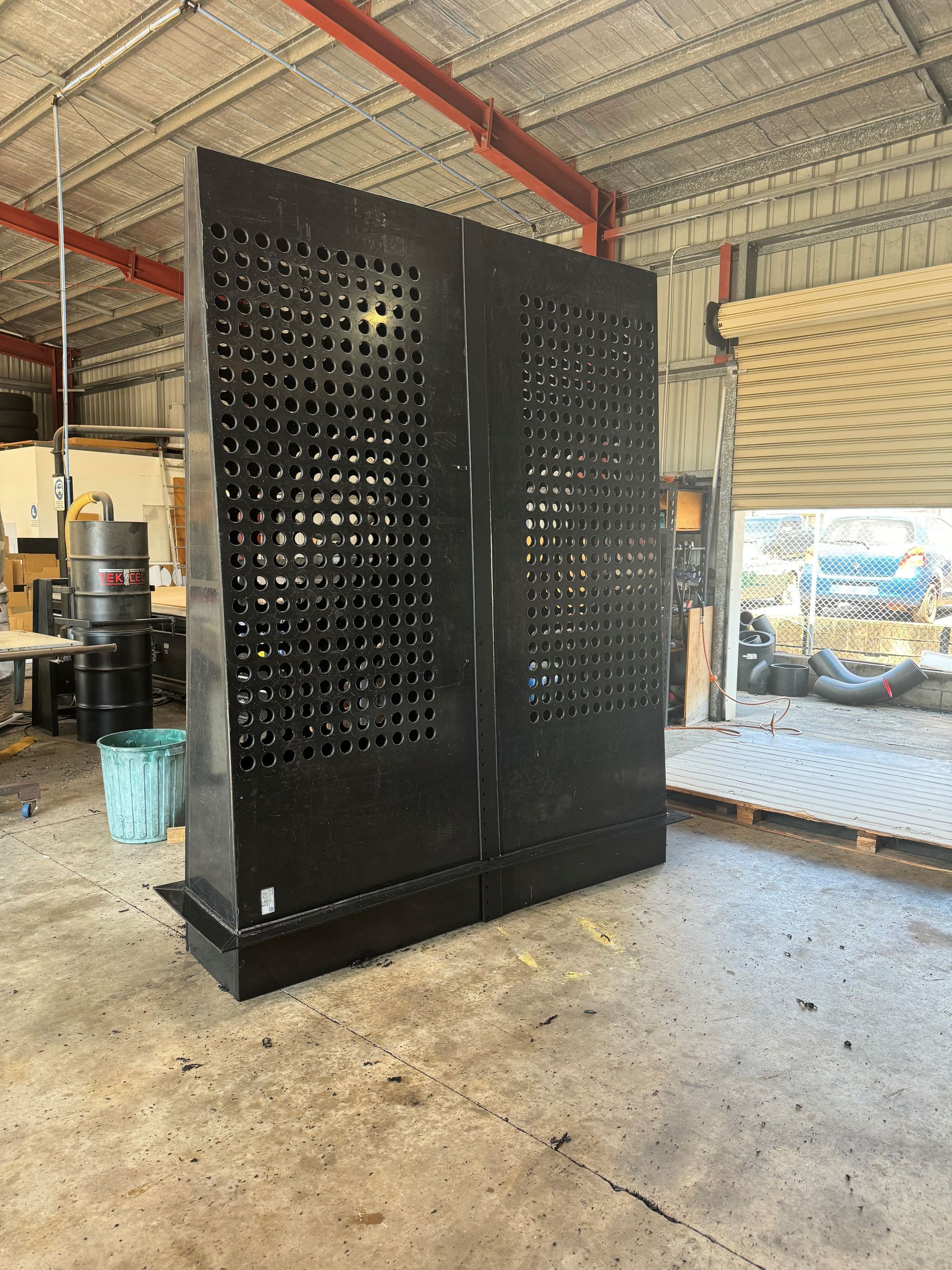 Black perforated metal partition/panel in an industrial workshop with a concrete floor and corrugated roof. — Advanced Poly in Darwin, NT — Advanced Poly in Darwin, NT 