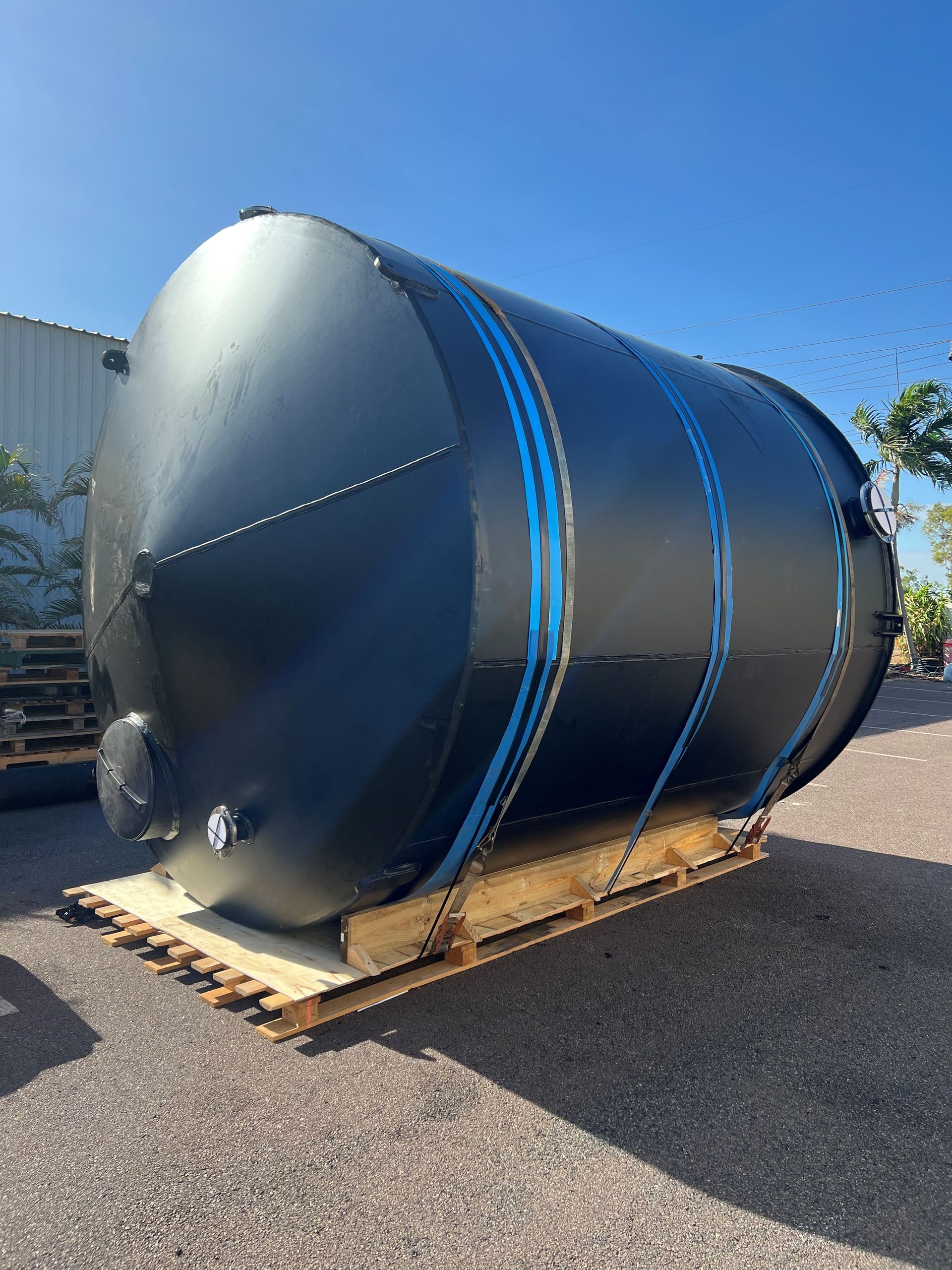 Large black cylindrical tank on a wooden pallet outdoors under a clear blue sky. — Advanced Poly in Darwin, NT 
