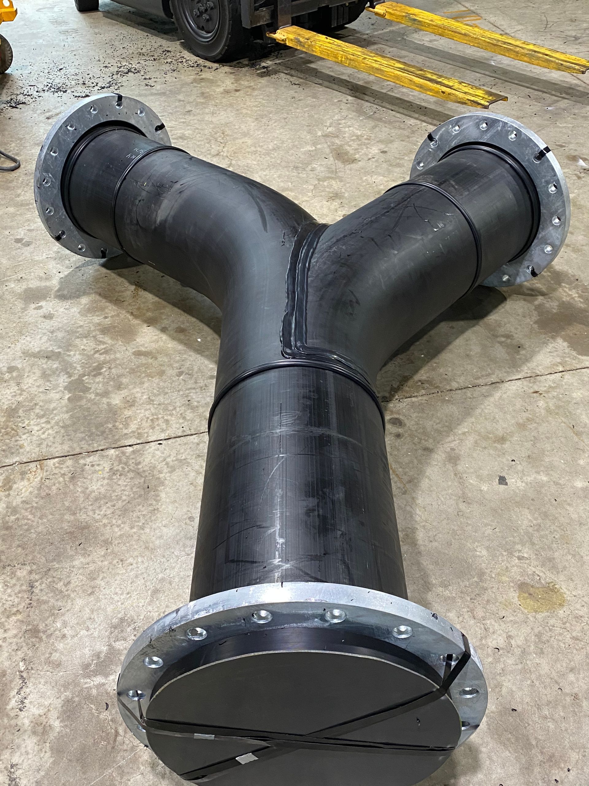Black Y-shaped metal pipe assembly with flanged ends on a concrete floor — Advanced Poly in Darwin, NT