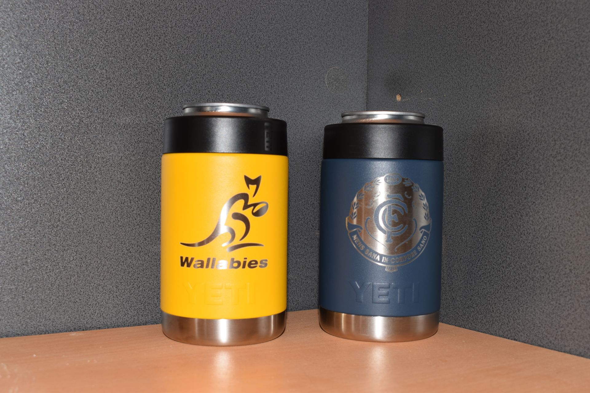 Two insulated drink coolers, yellow Wallabies and blue logo, standing on a wooden table — Advanced Poly in Darwin, NT