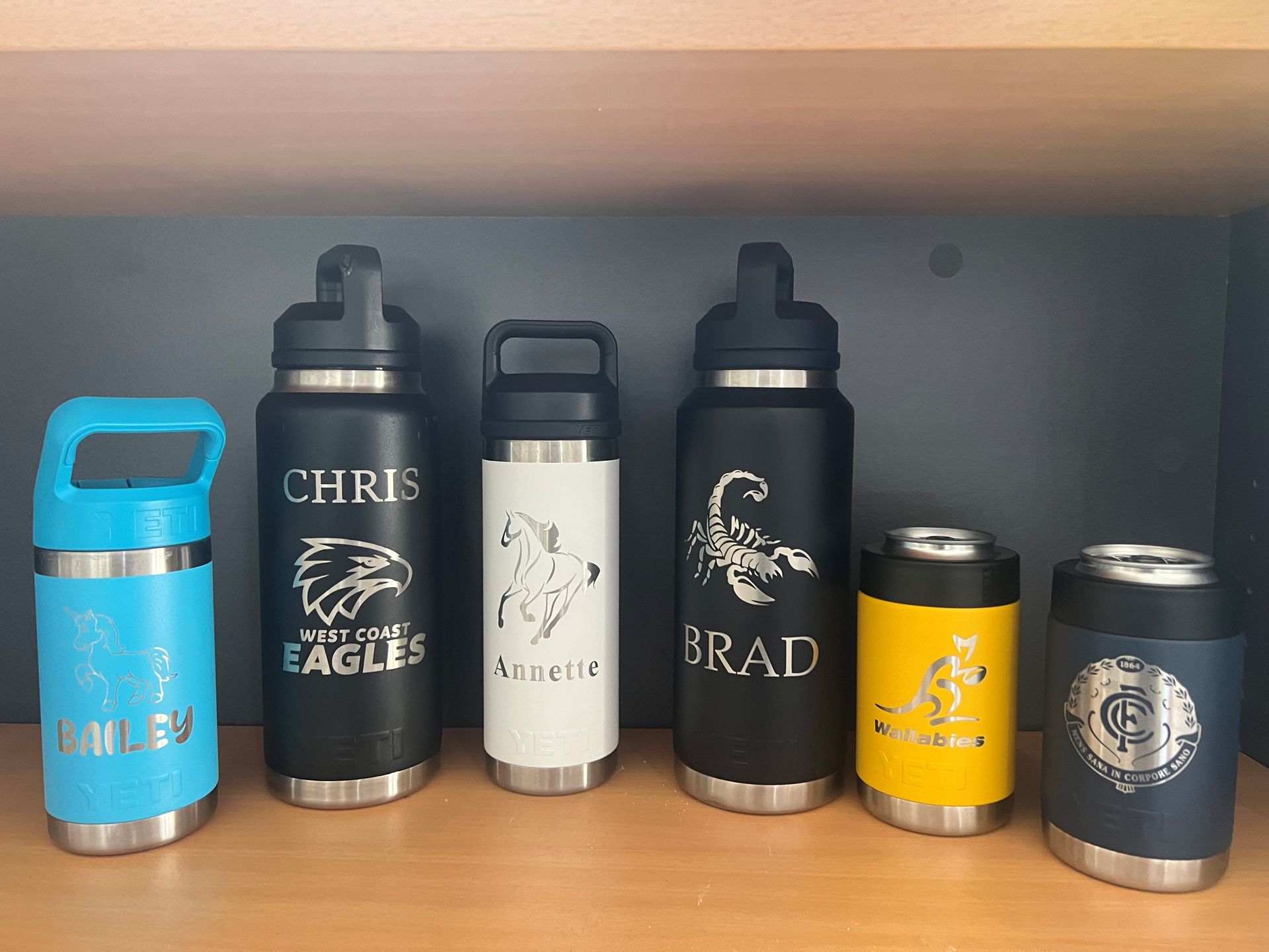 Assorted personalized insulated drink tumblers on a shelf, in blue, black, white, yellow, and navy. — Advanced Poly in Darwin, NT
