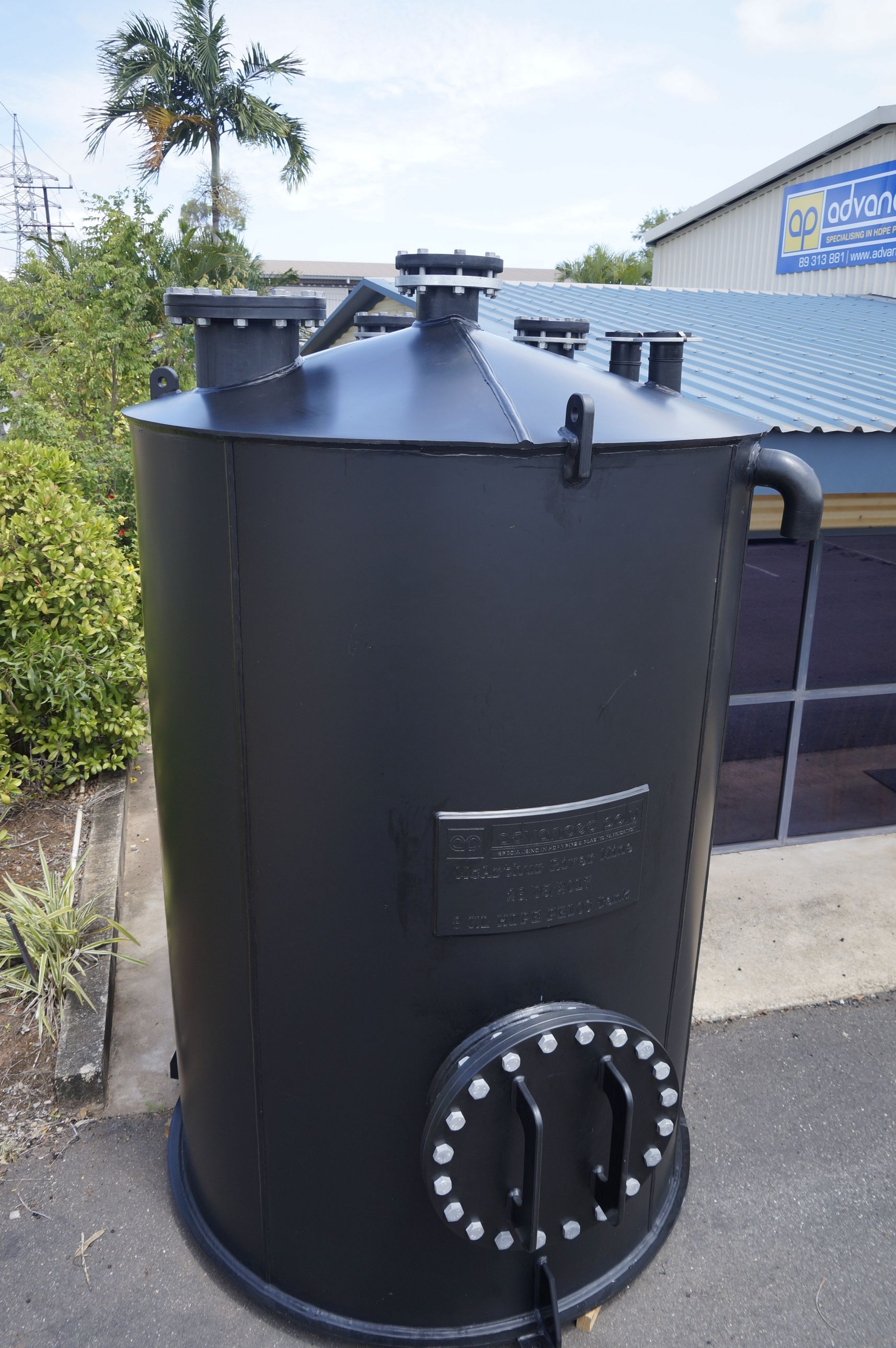 Black cylindrical water tank beside a house, with a ladder and lid fittings on top. — Advanced Poly in Darwin, NT