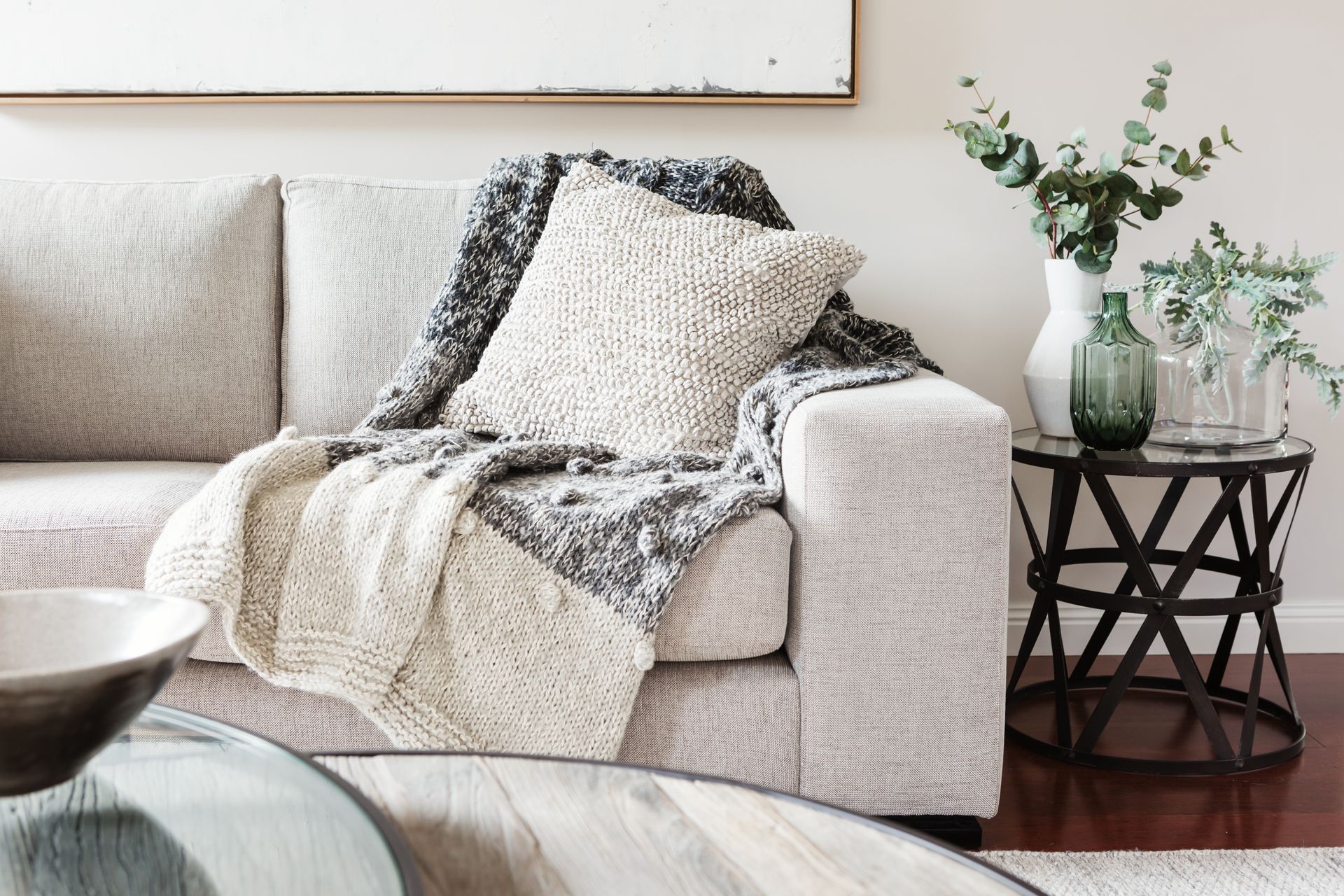 Beige sofa with cream and gray knitted blanket and pillow; small table with greenery.