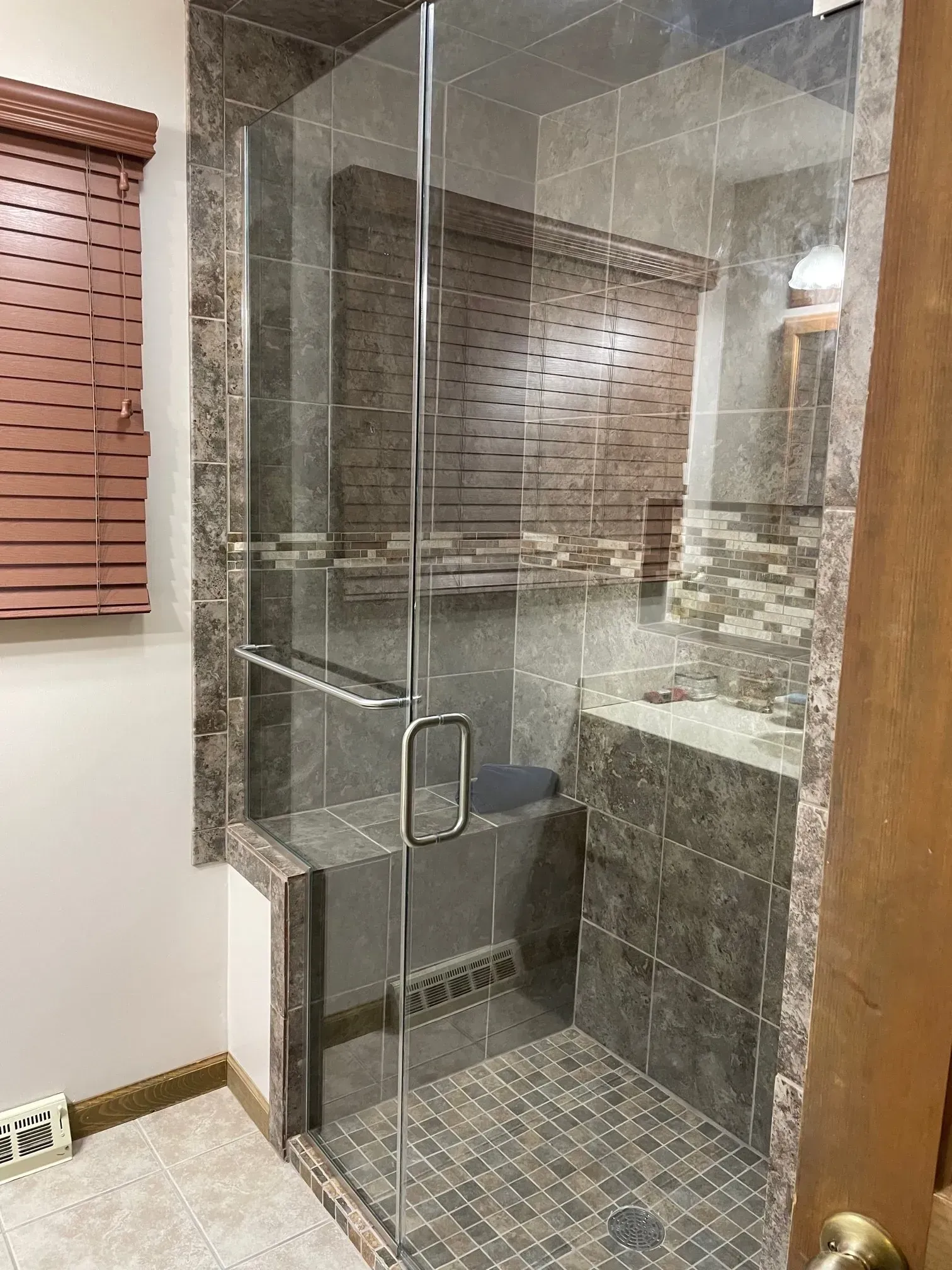Glass shower enclosure with gray tile walls and floor in a bathroom.