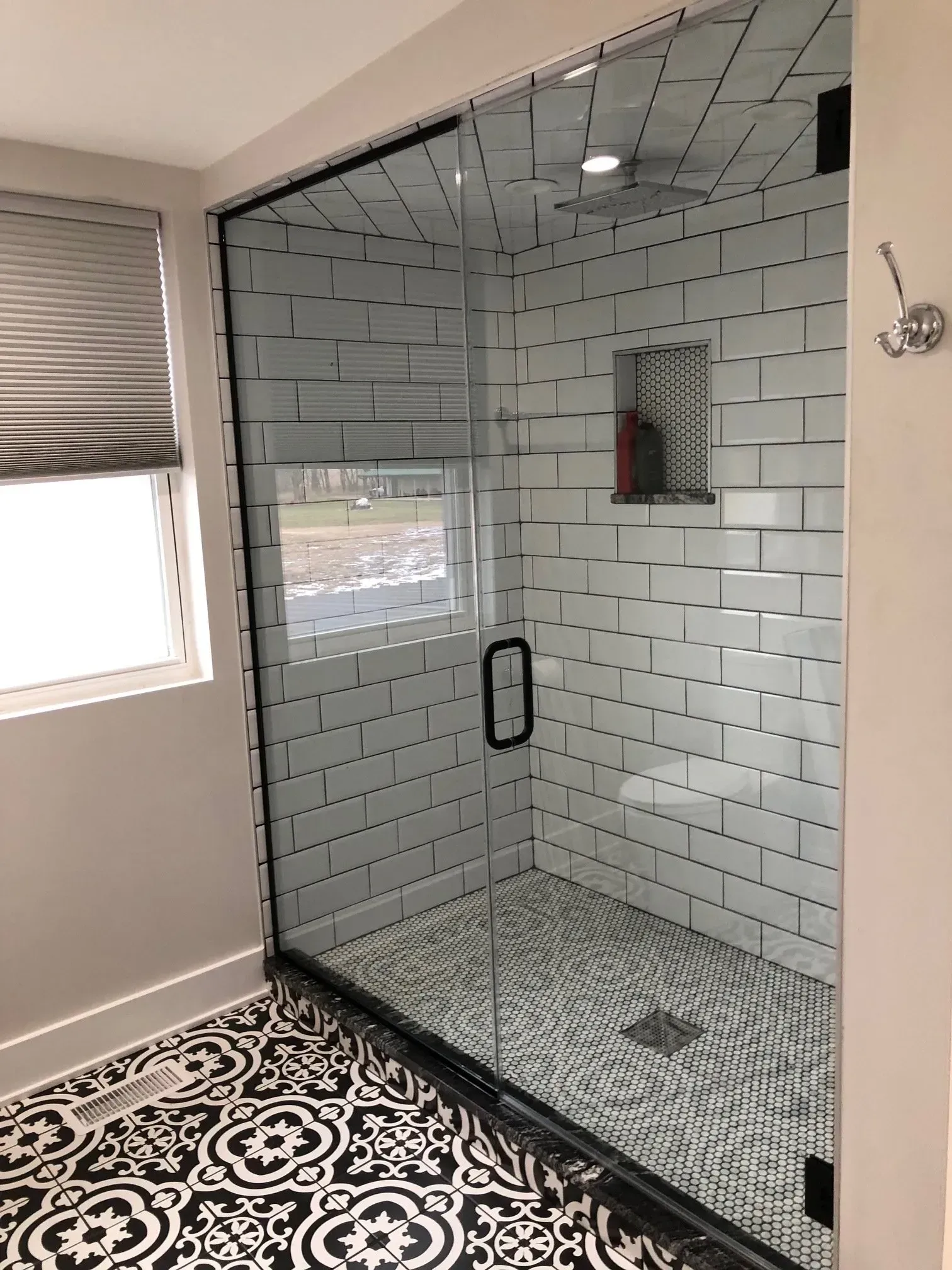 Glass shower enclosure with white subway tiles and patterned floor in a bright bathroom
