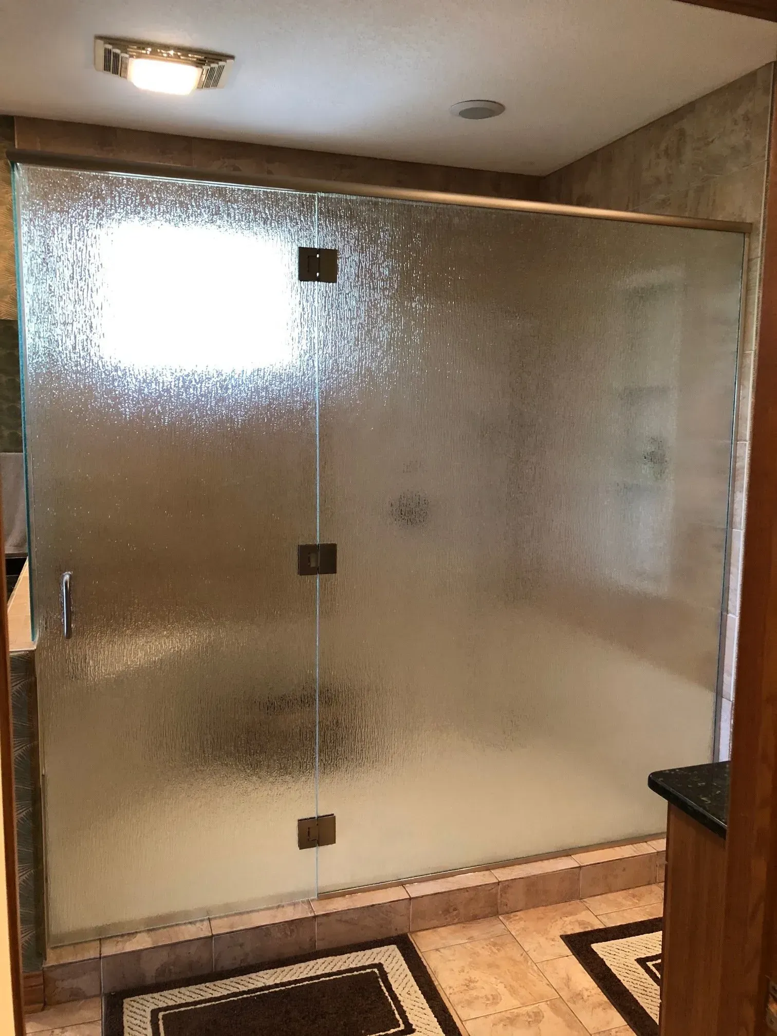 Frosted glass shower enclosure in a bathroom with beige tile and black floor trim