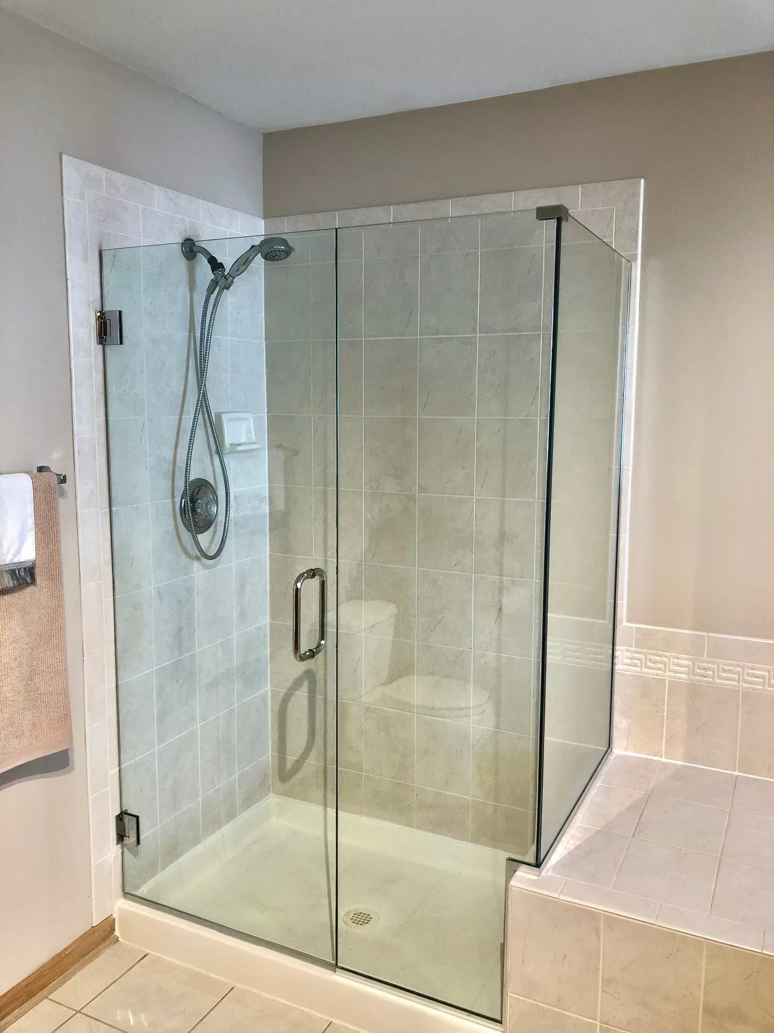 Glass shower enclosure with tiled walls and a handheld showerhead in a beige bathroom