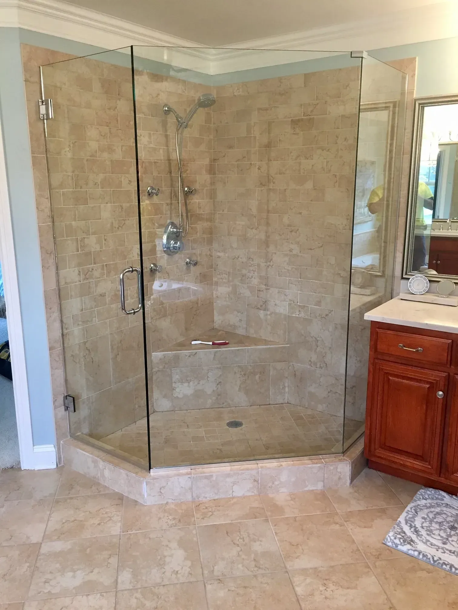 Glass-enclosed corner shower with beige tile and chrome fixtures in a bathroom