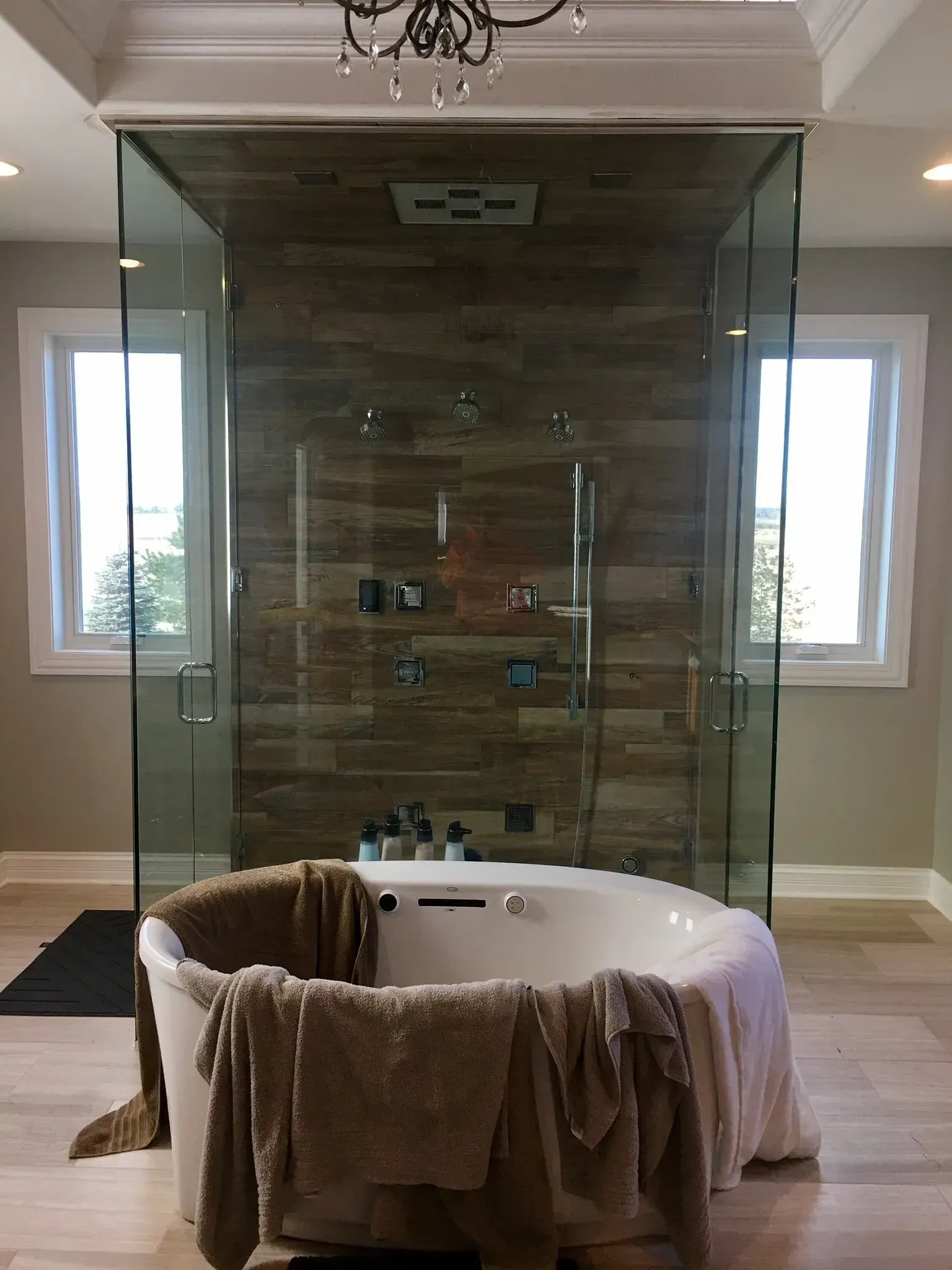 Freestanding bathtub with towel inside a glass-enclosed bathroom, flanked by two windows.