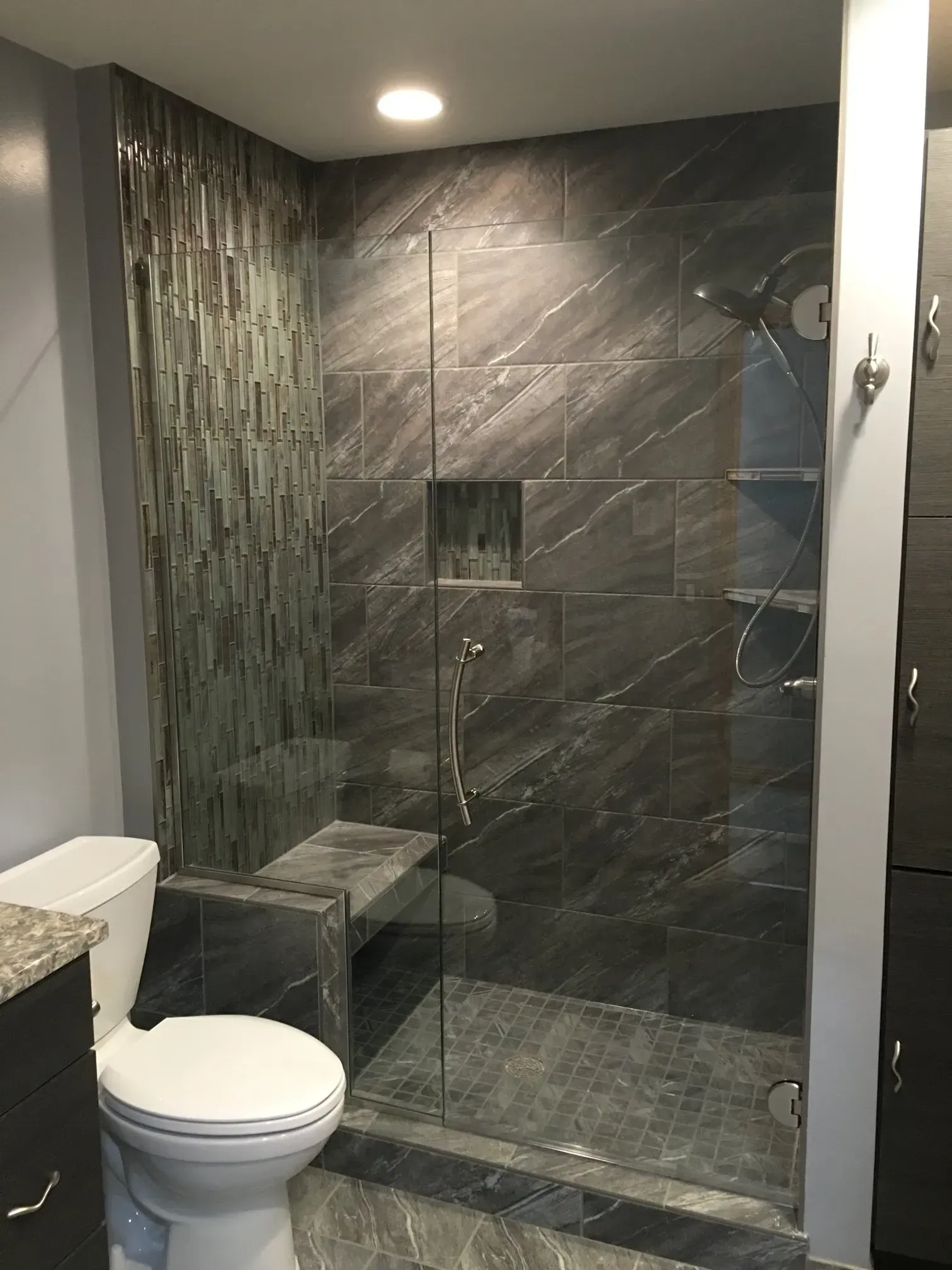 Modern bathroom with dark tiled walk-in shower and a toilet in the foreground