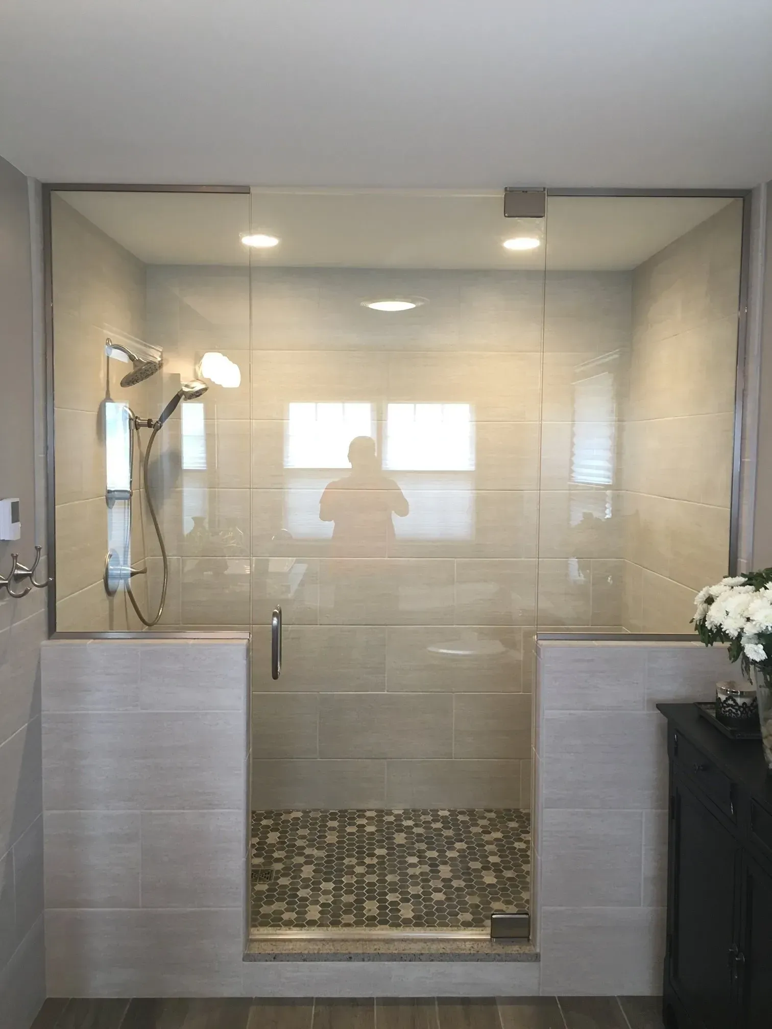 Modern glass shower enclosure with wall-mounted showerhead and mosaic tile floor in a tiled bathroom