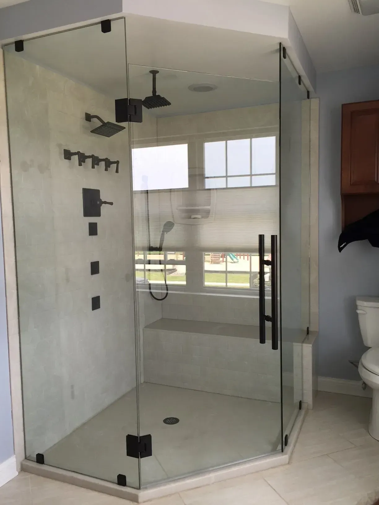Corner glass shower enclosure in a modern bathroom with black fixtures and white tile floor
