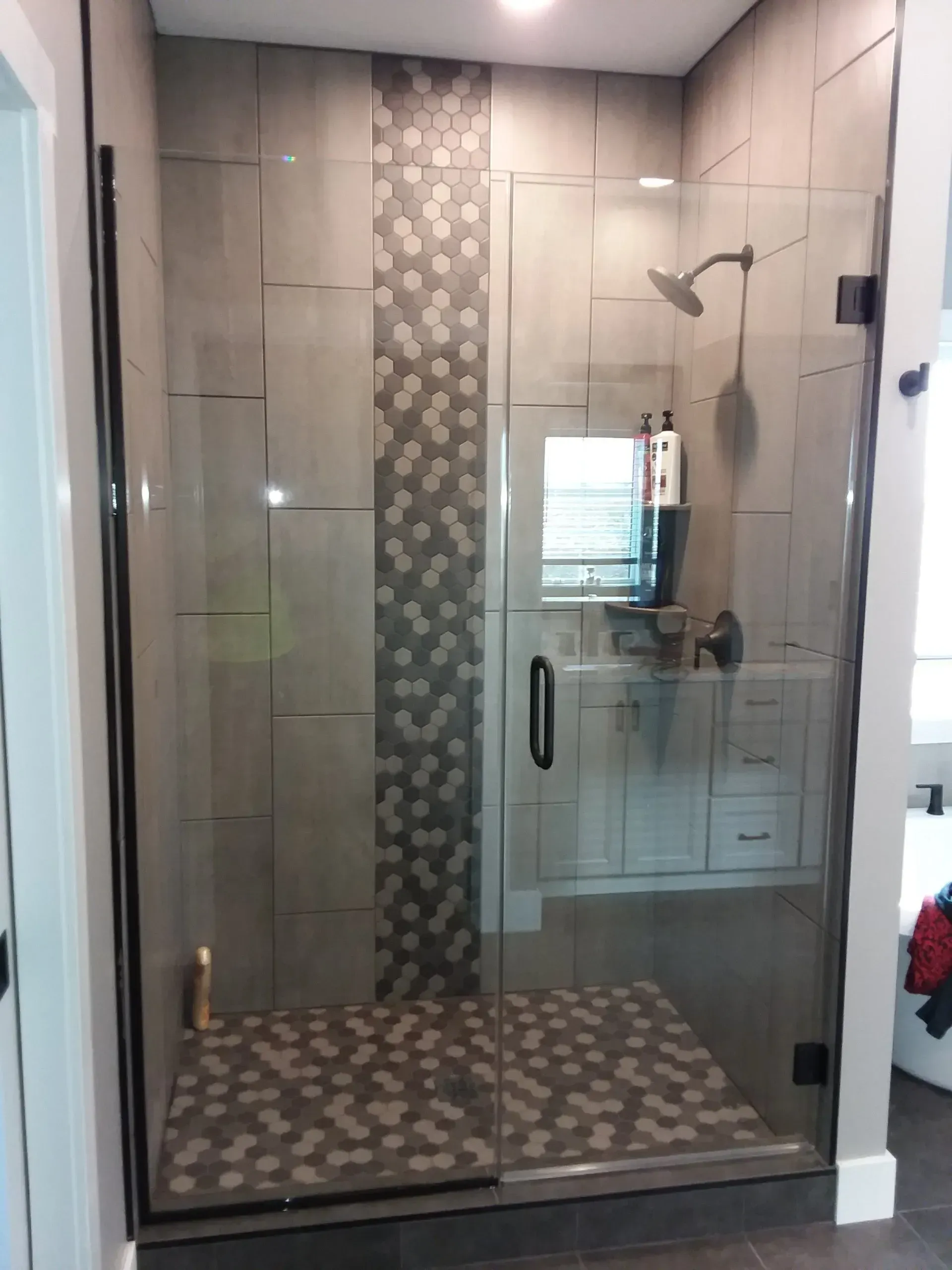 Glass walk-in shower with gray mosaic tile floor and vertical accent strip, chrome fixtures, and beige walls