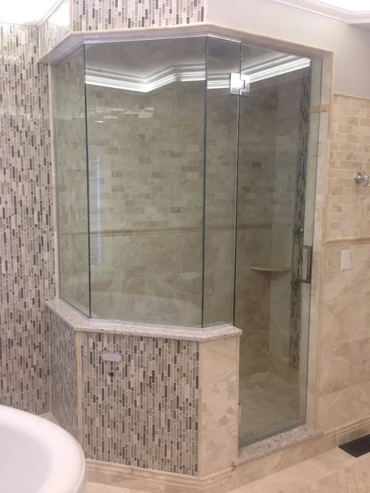 Glass-enclosed corner shower with tiled walls in a bathroom