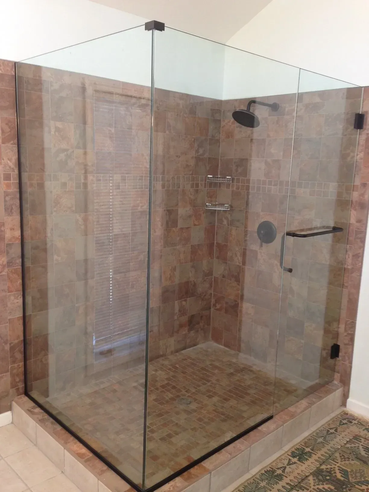 Glass-enclosed tiled walk-in shower with beige stone walls and floor