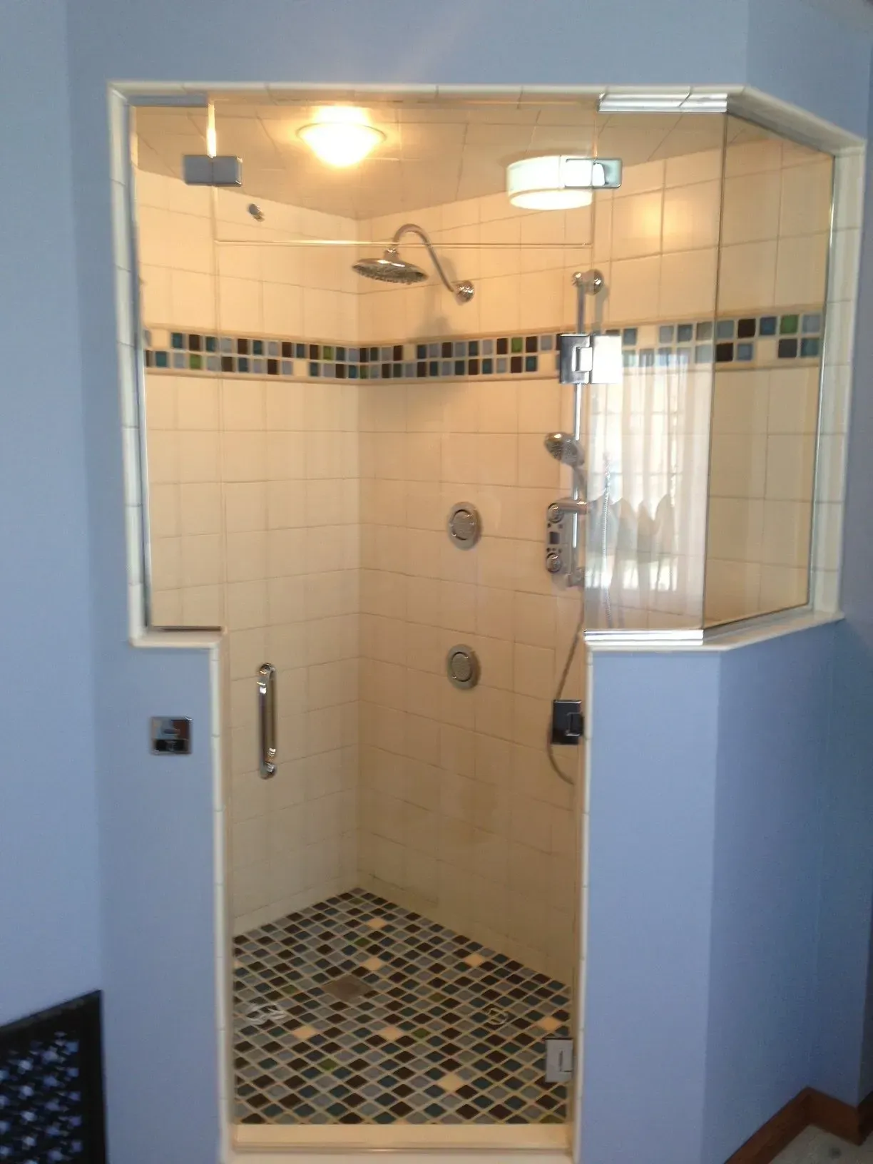 Glass-enclosed shower with beige tile walls and mosaic floor in a bathroom