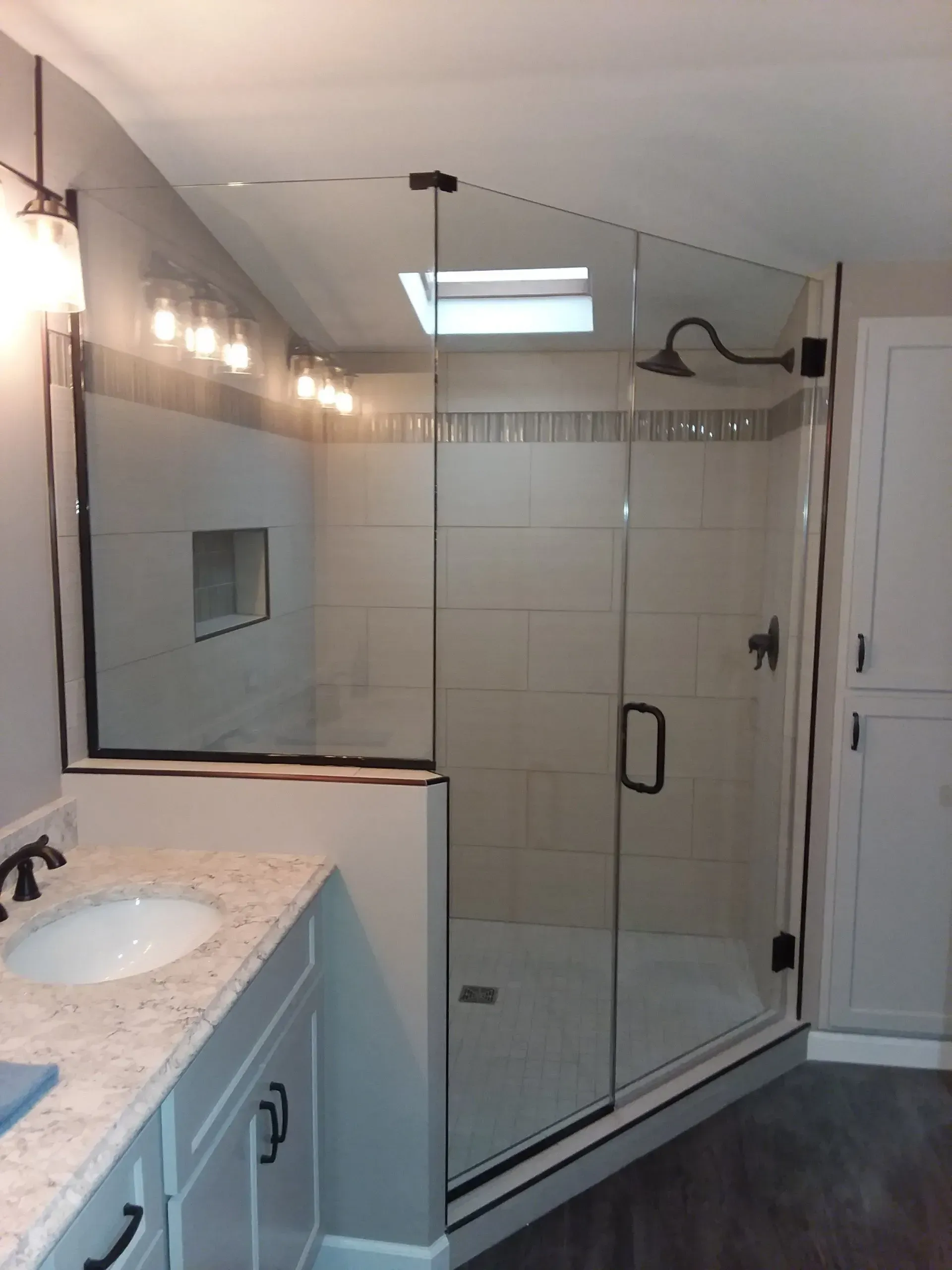 Bathroom with glass shower enclosure, granite vanity, and wall lights over a sink.