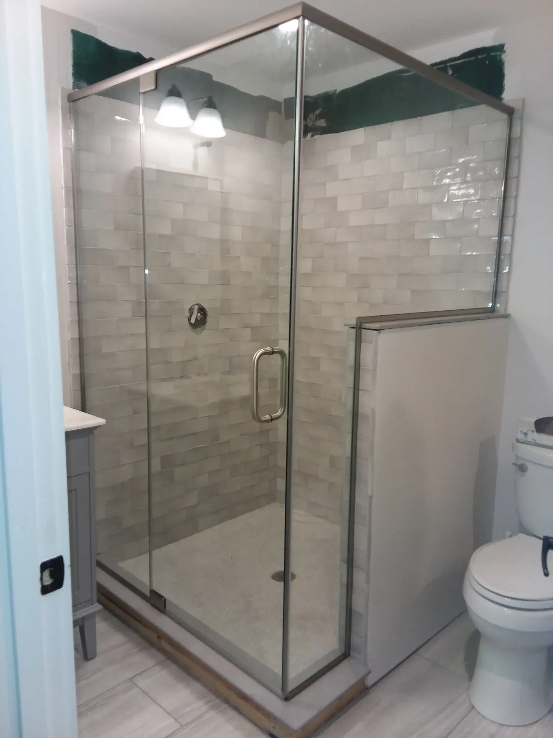 Modern tiled walk-in shower with glass doors beside a toilet in a bathroom