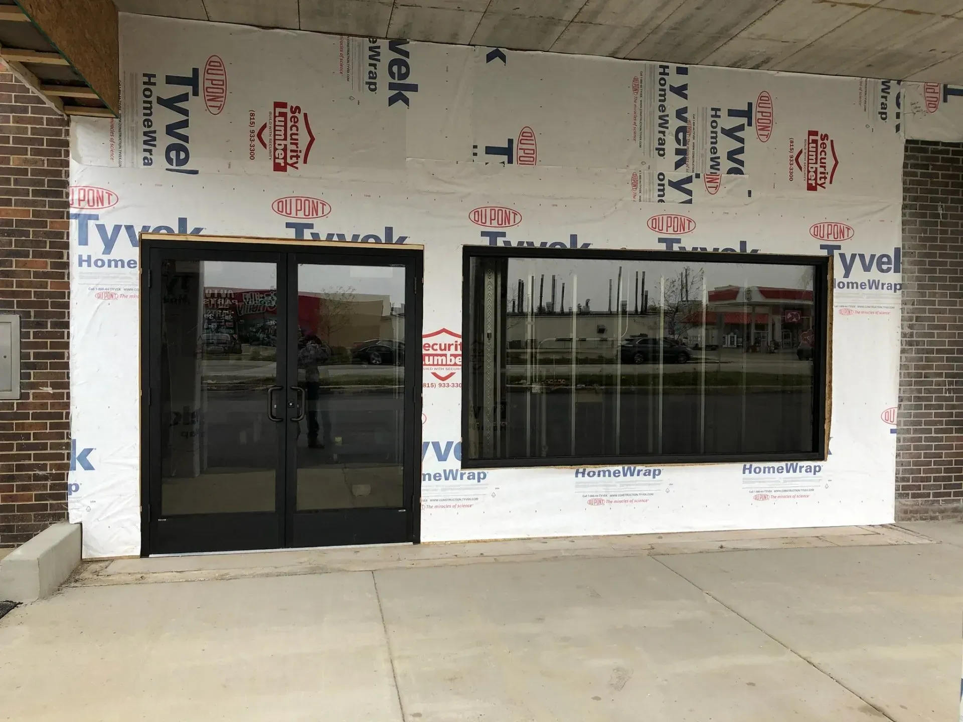 Storefront under construction with black-framed glass doors and window, wrapped in Tyvek house wrap.