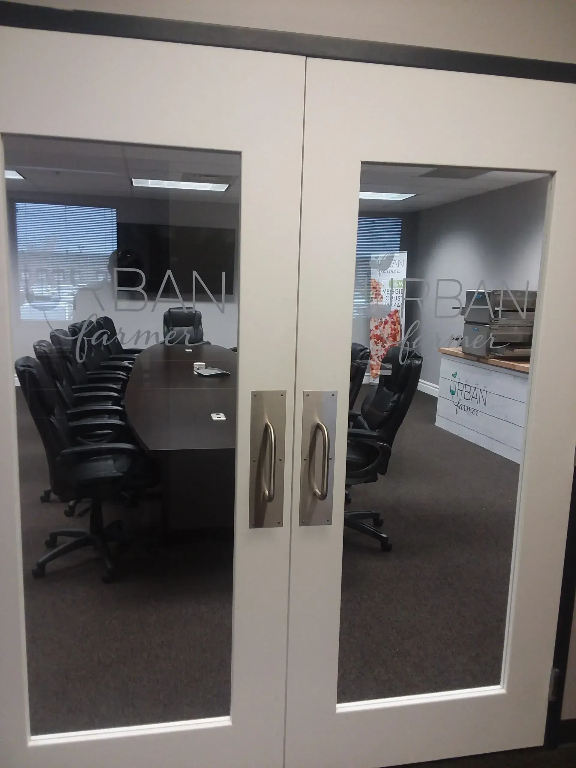 Glass office doors with metal handles, showing a conference room with chairs and desks inside
