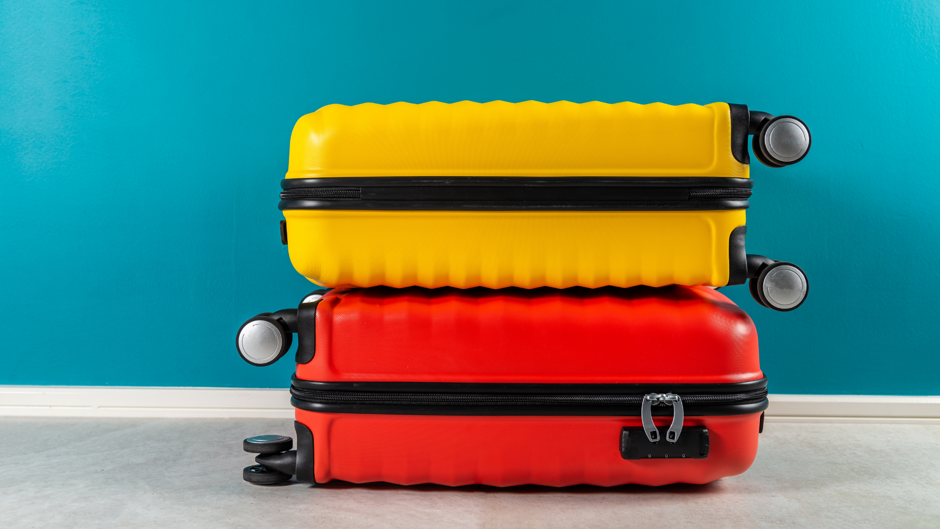 Two stacked suitcases, yellow on red, against a turquoise wall.