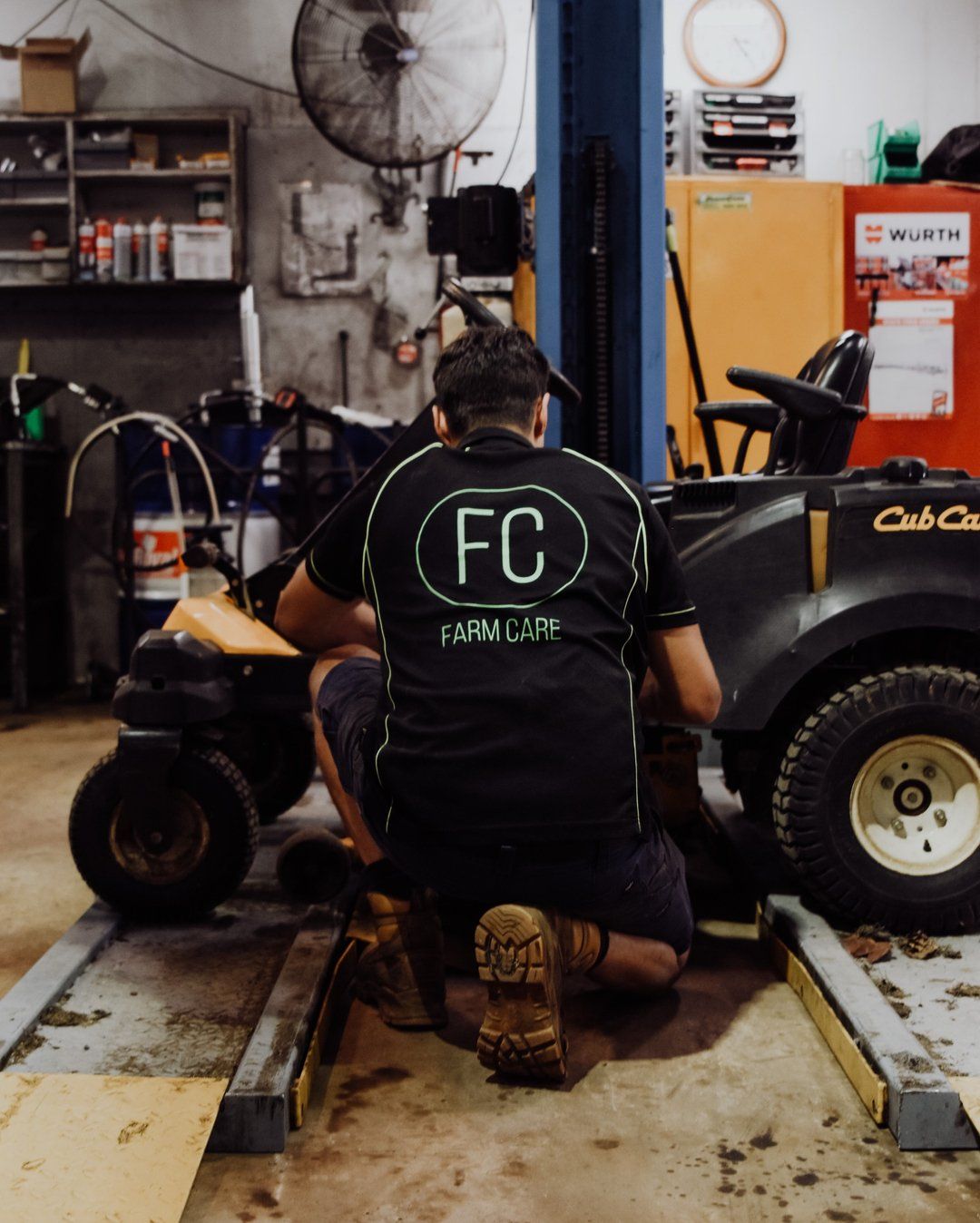A Man Wearing a Black Shirt That Says Fc is Working on a Lawn Mower — FarmCare in Mullumbimby, NSW