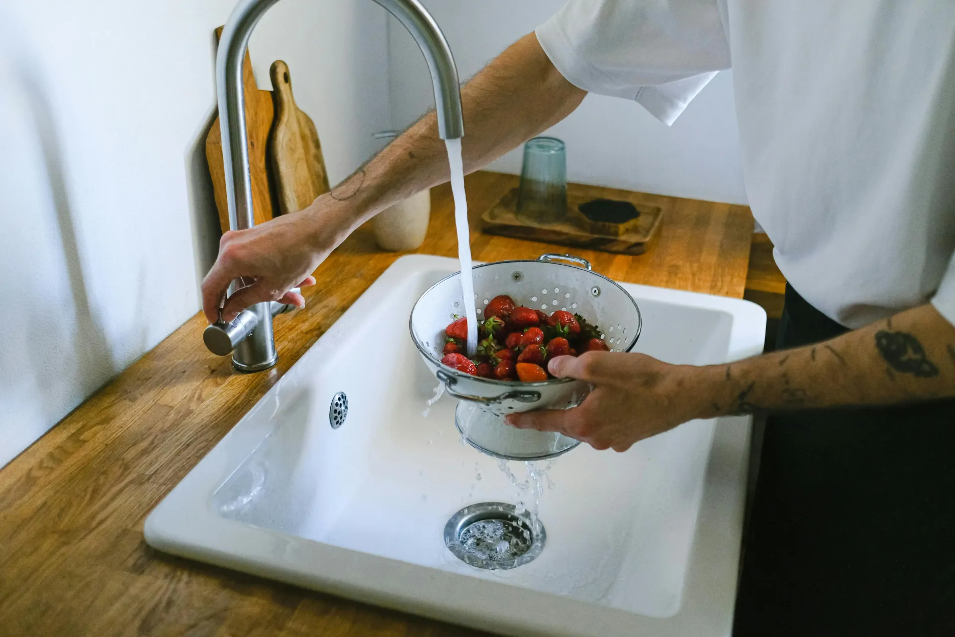 A person is washing strawberries in a bowl in a kitchen sink.