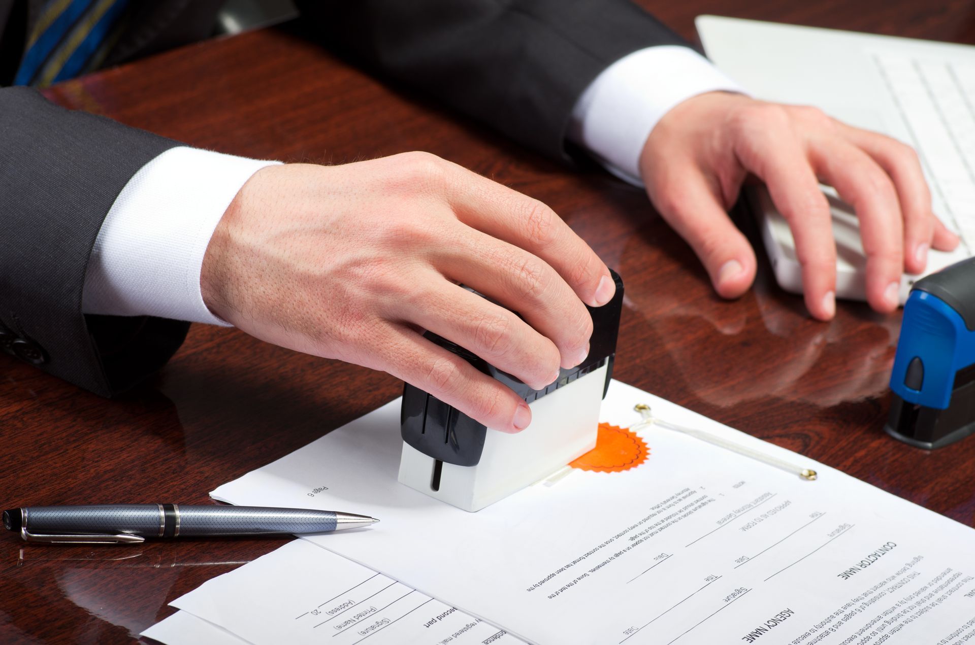 A person in a suit stamps a document with a seal at a desk