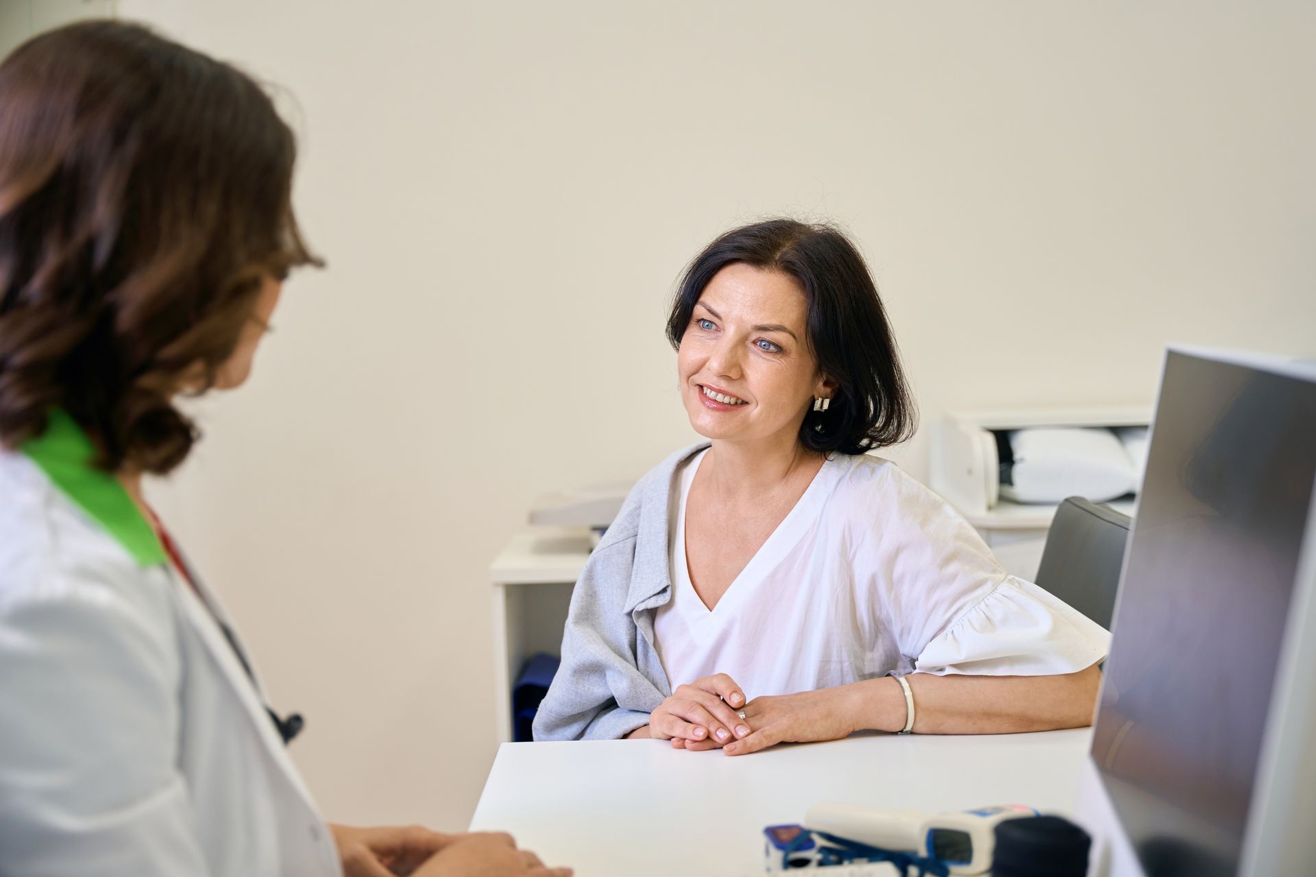 A woman is sitting at a desk talking to a doctor.
