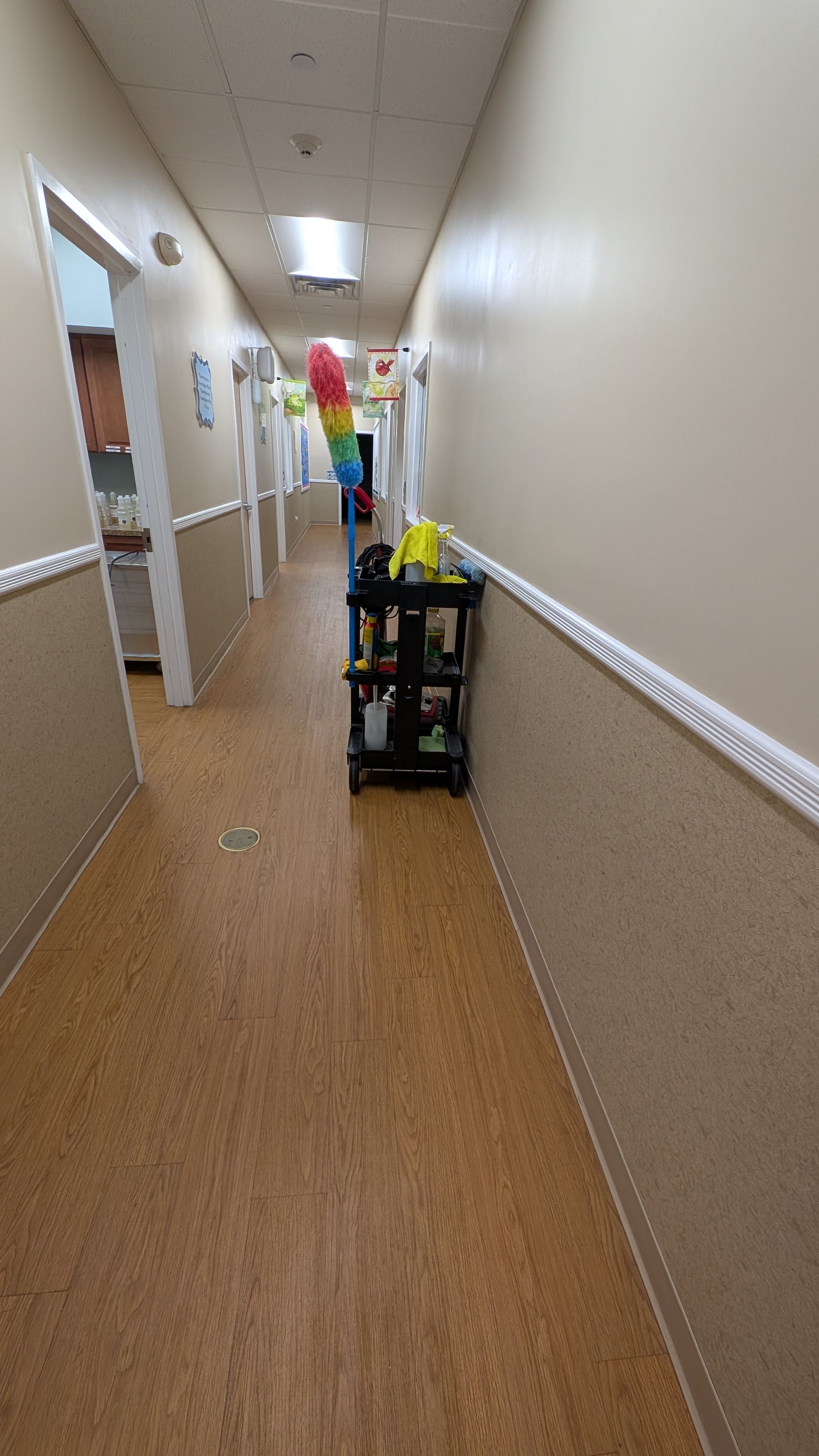 Long hallway with beige walls, fluorescent lights, and a cleaning cart near the center.