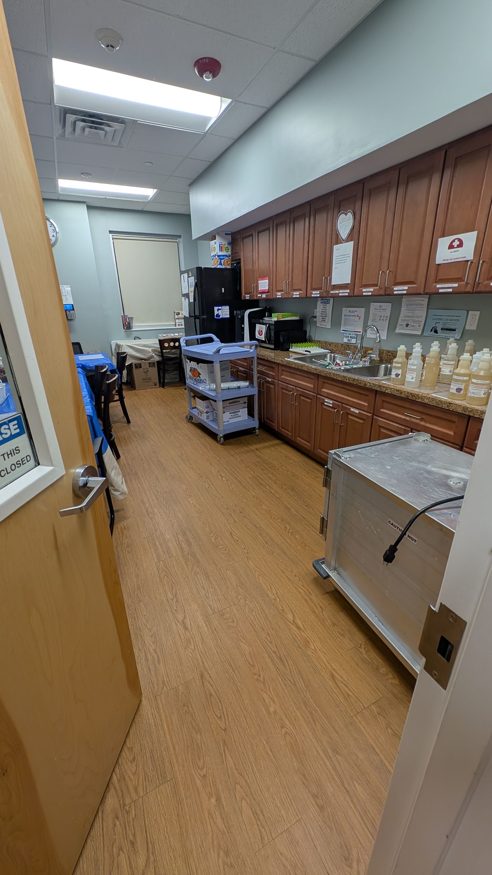 Narrow clinic hallway with wood cabinets, countertop supplies, and a cart under bright fluorescent lights