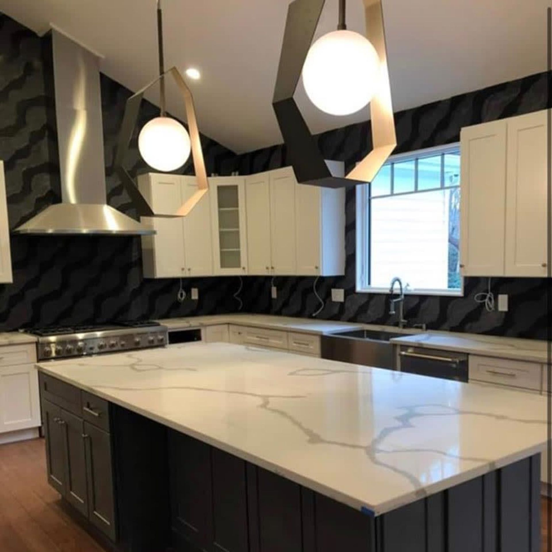 Modern kitchen with large white island, dark cabinets, pendant lights, and geometric black backsplash
