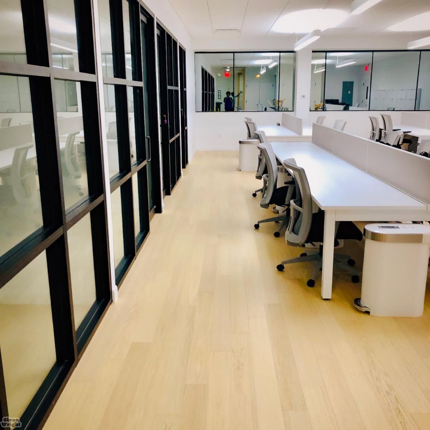 Modern open-plan office with desks, monitors, chairs, and large windows with natural light