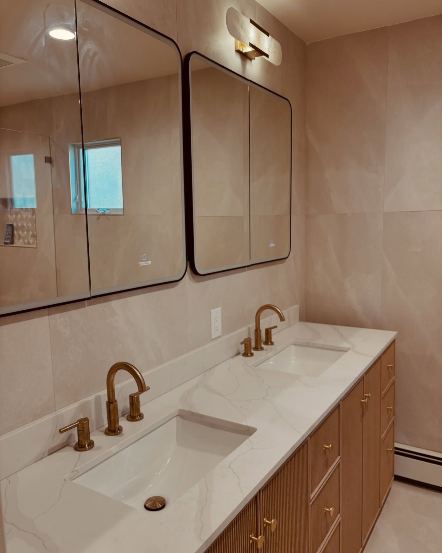 Modern bathroom vanity with double sinks, gold faucets, and large wall mirrors
