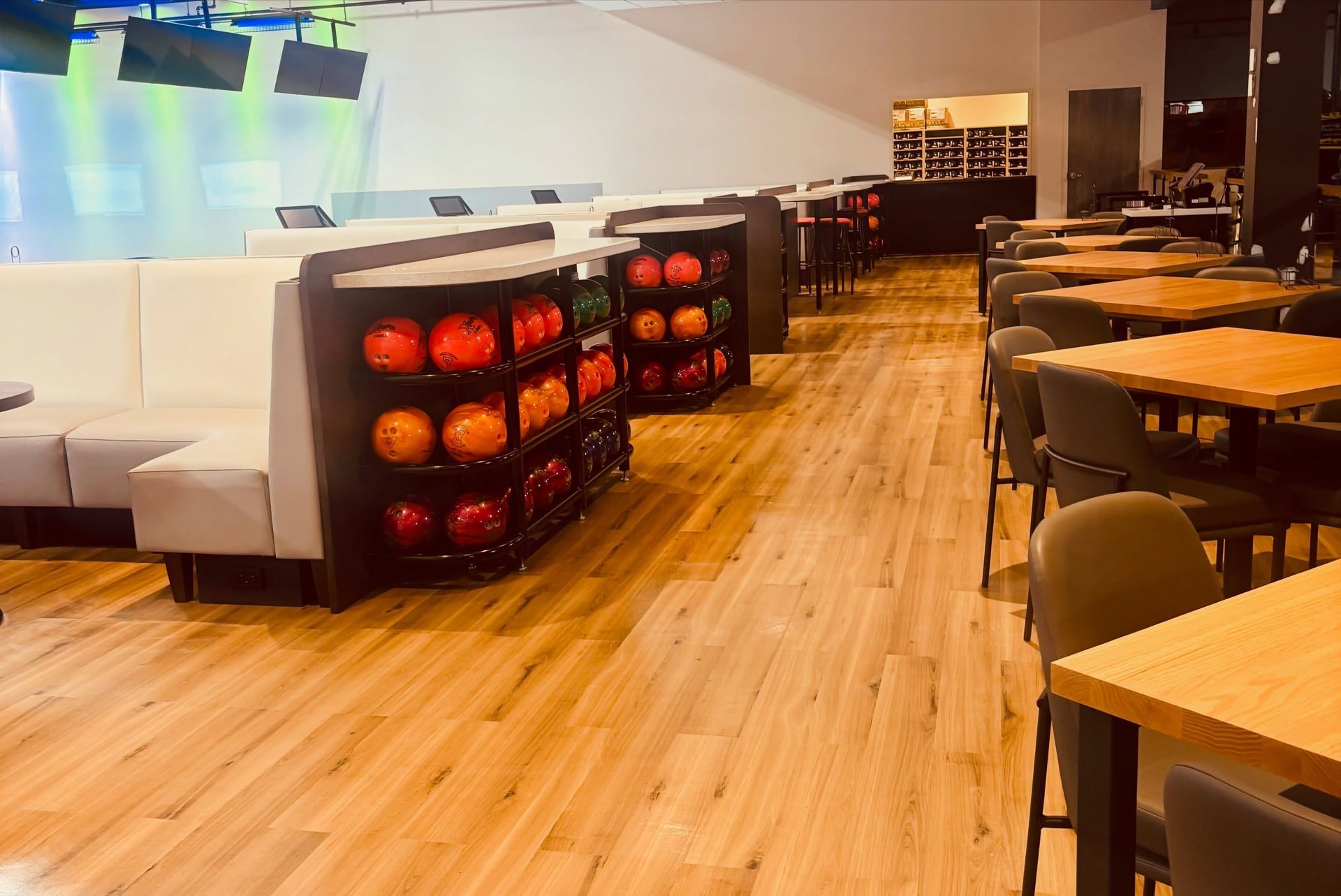 Bowling alley lounge with white couches, ball racks, and tables along a wooden floor