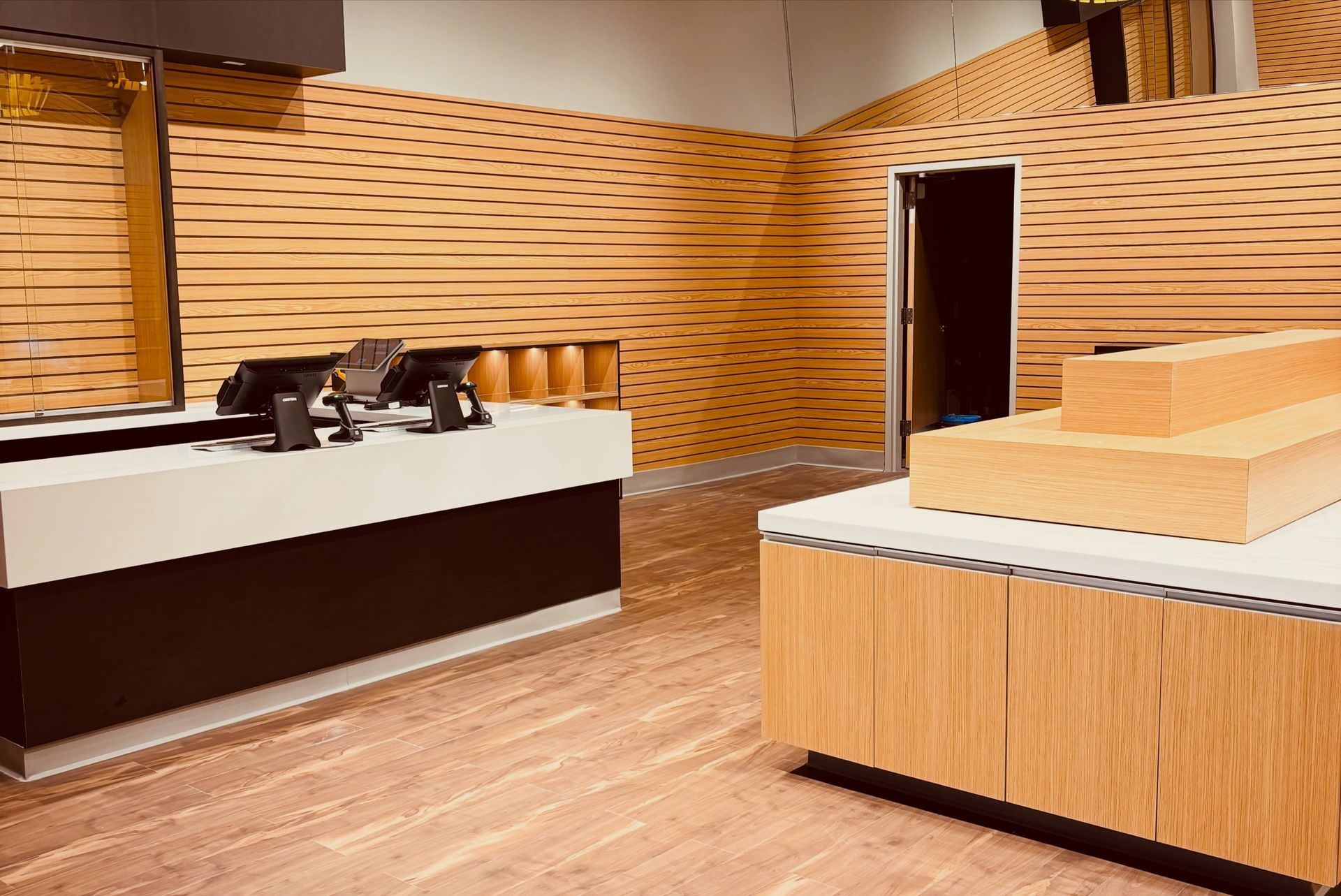 Modern retail or service counter interior with wood paneling, display tables, and a doorway at the back