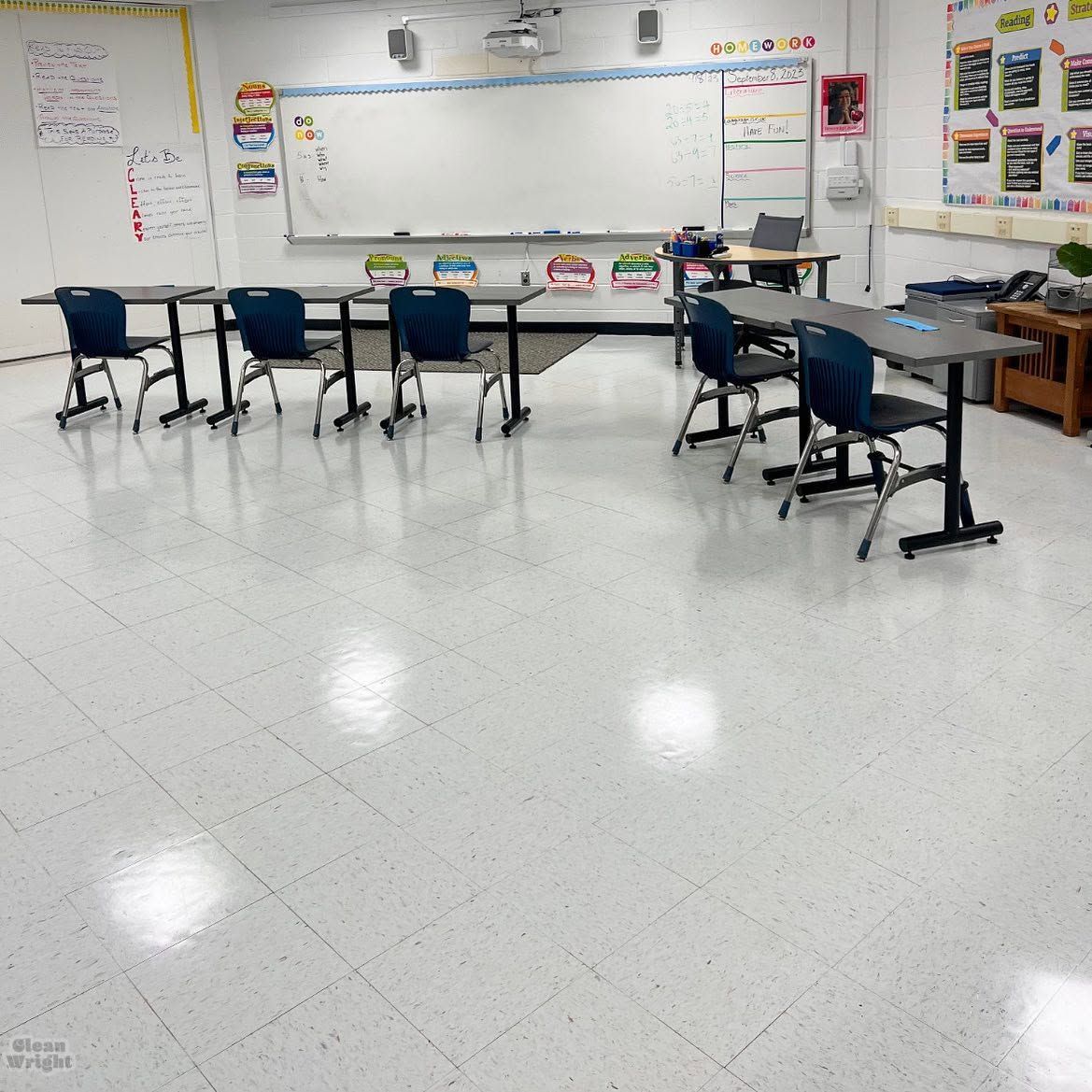 Empty classroom with blue chairs, wooden desks, large windows, and a whiteboard on the front wall.