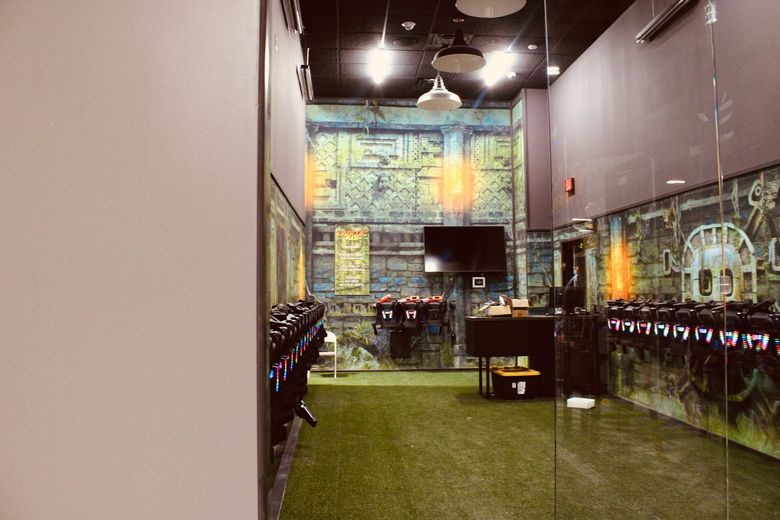 Indoor sports facility with green turf, tall netted walls, and a TV screen at the far end